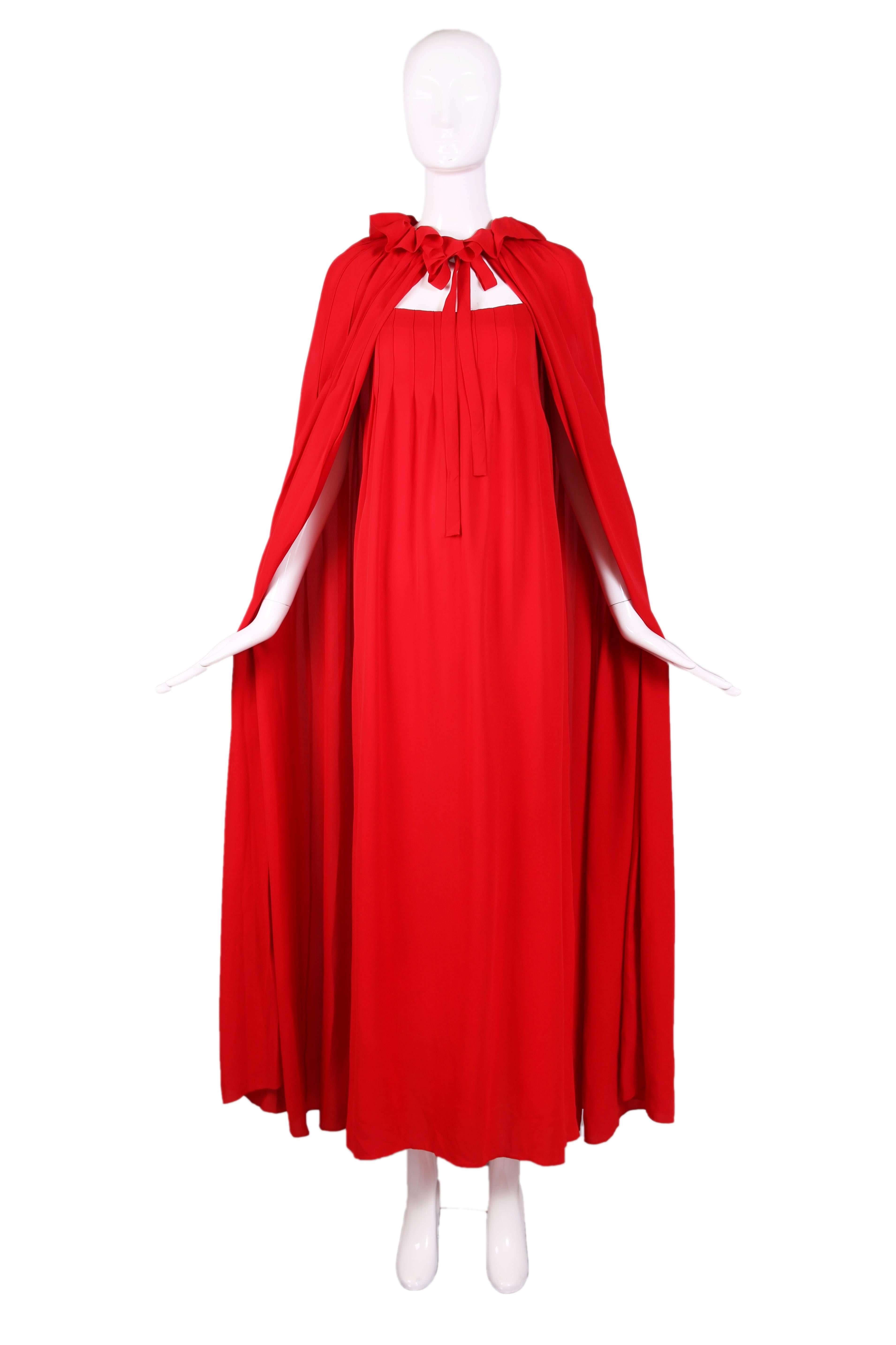 1970 Christian Dior haute couture red silk maxi dress and cape ensemble. Cape has a ruffle neckline with neck tie. Dress has spaghetti straps and there is pleating at bust on both dress and cape. In excellent vintage condition with some assorted