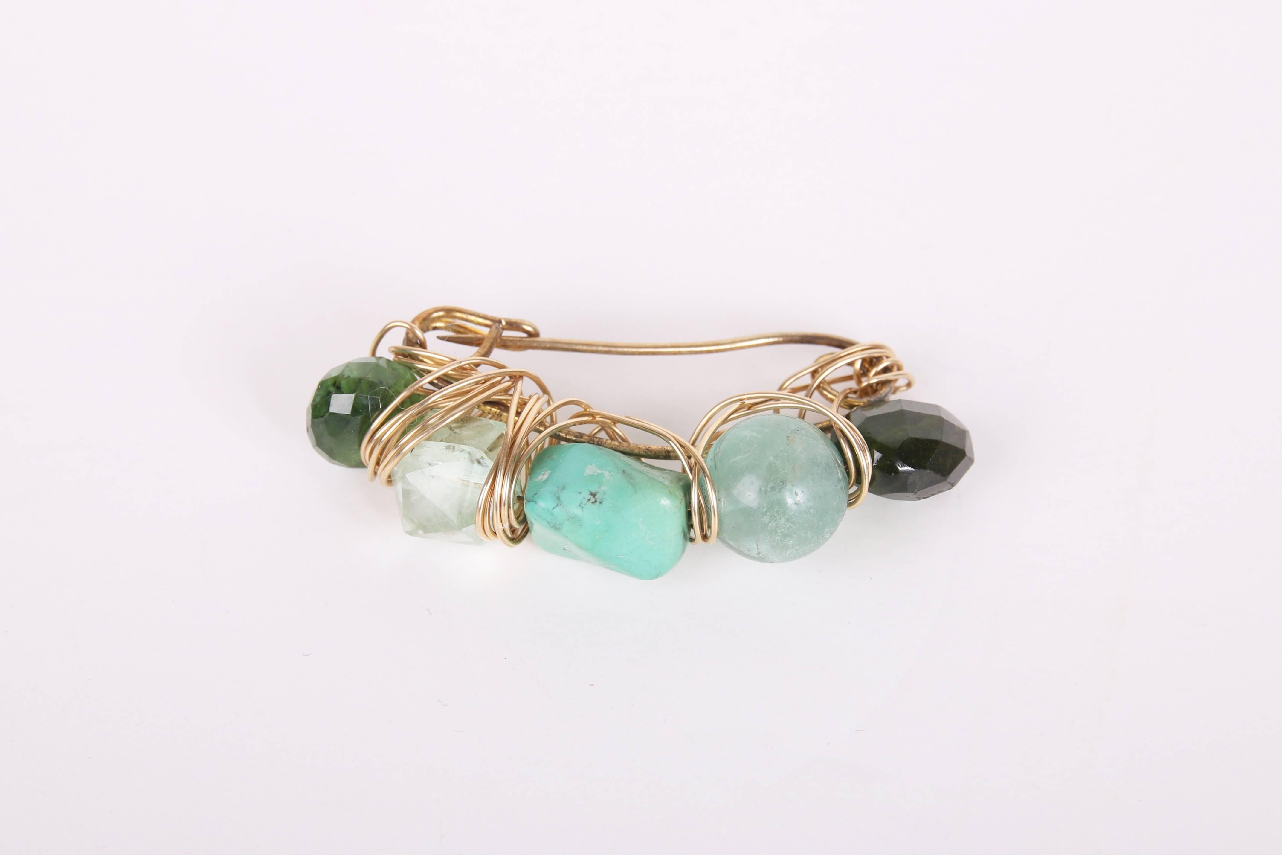 Kazuko 14k gold wire wrapped brooch made from semi-precious gemstone beads on a safety pin. Each of the five beads appear to be a different kind of stone - while all in the green/blue family. And in a variety of finishes - faceted, smooth, tumbled,