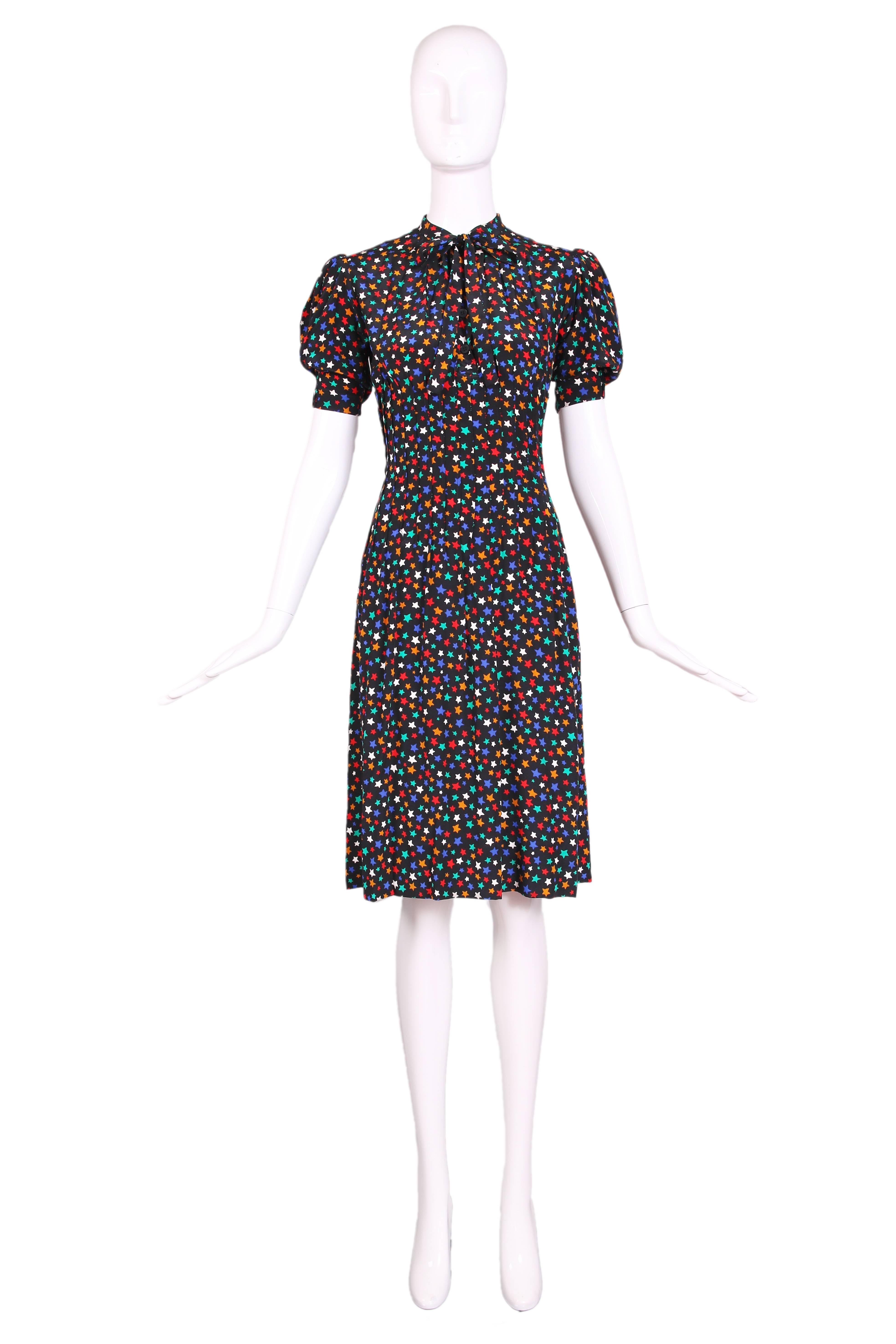 Vintage Yves Saint Laurent black silk day dress with a star print in white, red, orange, blue, and teal with neck ties, puffed short sleeves, and button front placket. The dress features pin tucking around waist area which turns into pleating at the