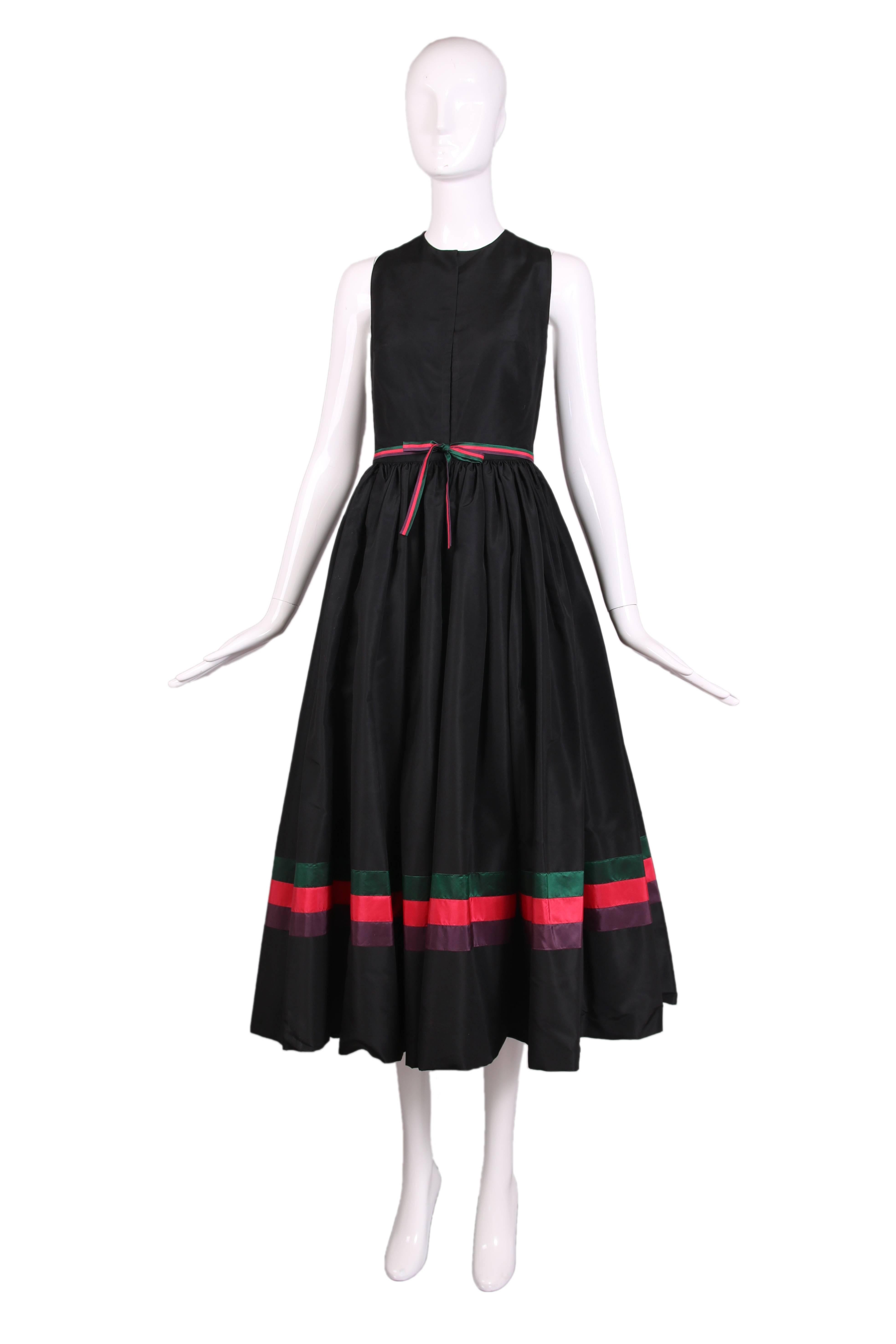 Vers 1983:: Madame Gres haute couture:: robe de cocktail sans manches en taffetas de soie noir avec un décolleté bijou:: un motif en forme de triangle renversé dans le dos et un couvre-chef noir sans manches assorti. La volumineuse jupe noire est