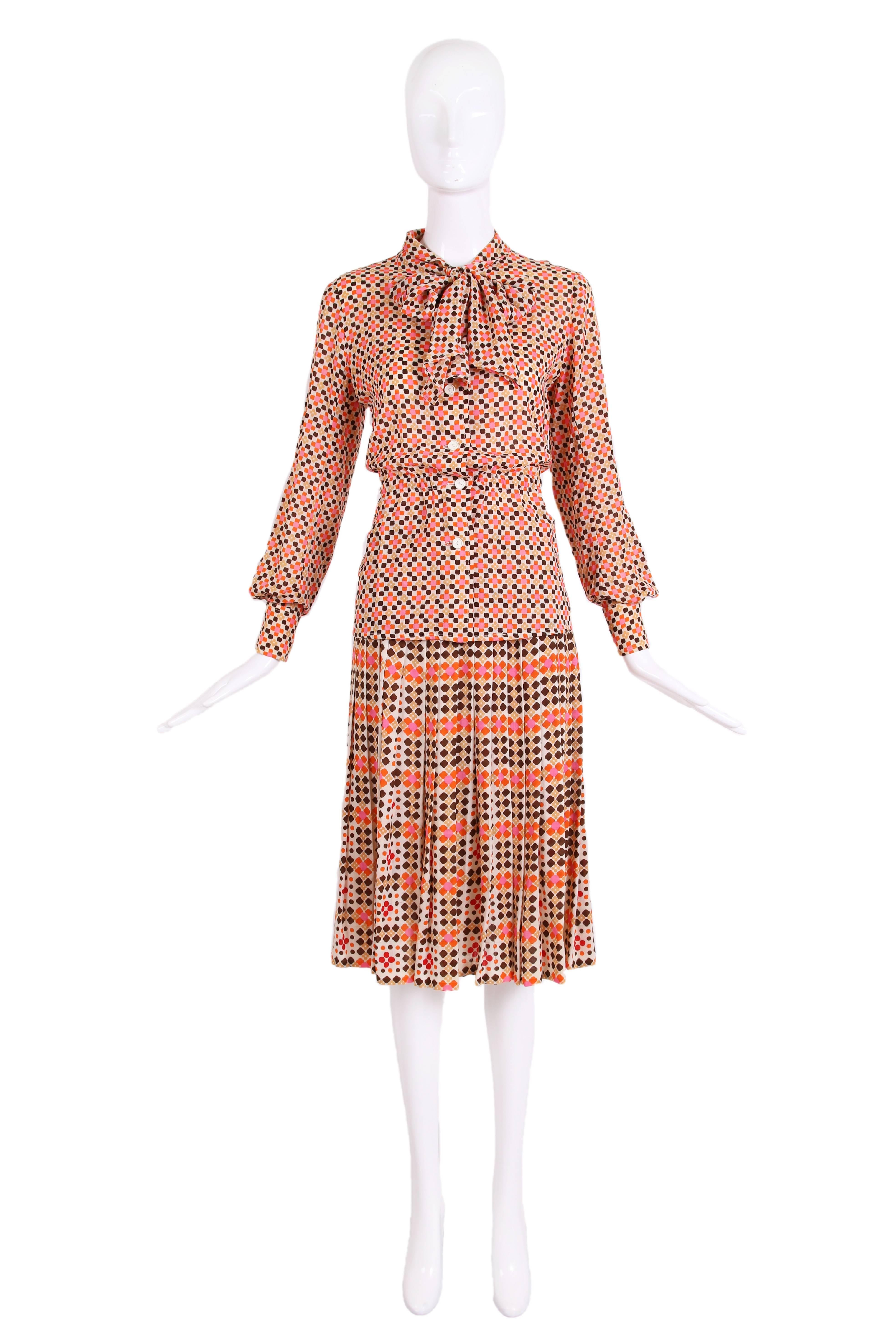 1970's Emanuel Ungaro geometric print two-piece blouse and pleated skirt ensemble in orange, yellow, pink, brown, and cream. Collared button down blouse with neck tie and cinching at the waist. Made from lightweight wool fabric. In excellent