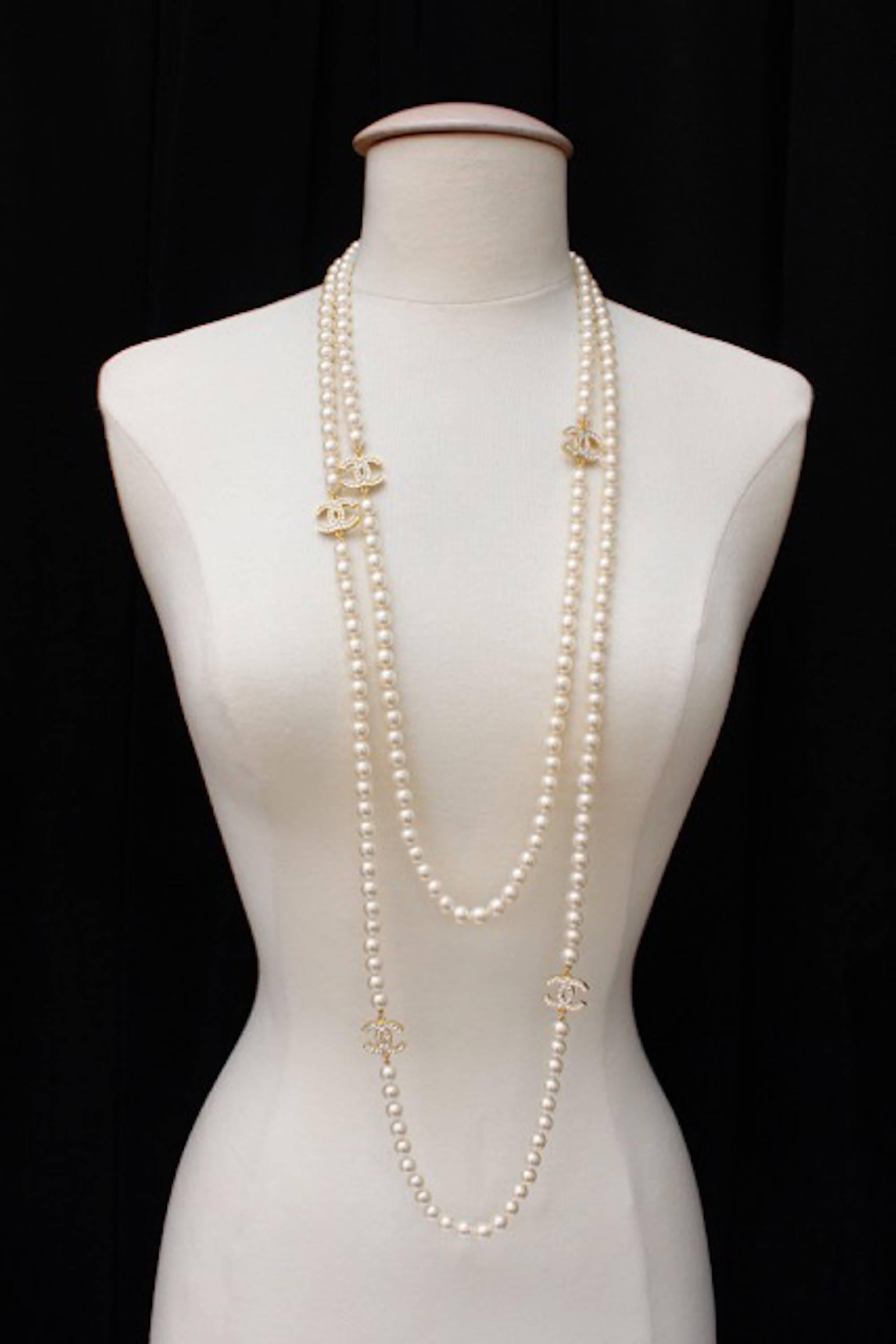 Authentic 2001 Chanel glass pearl extra long sautoir necklace with five alternating Swarovski crystal encrusted CC logos set in gold tone metal. Lobster claw clasp closure bearing the Chanel cartouche, stamped "Chanel 01A." In excellent