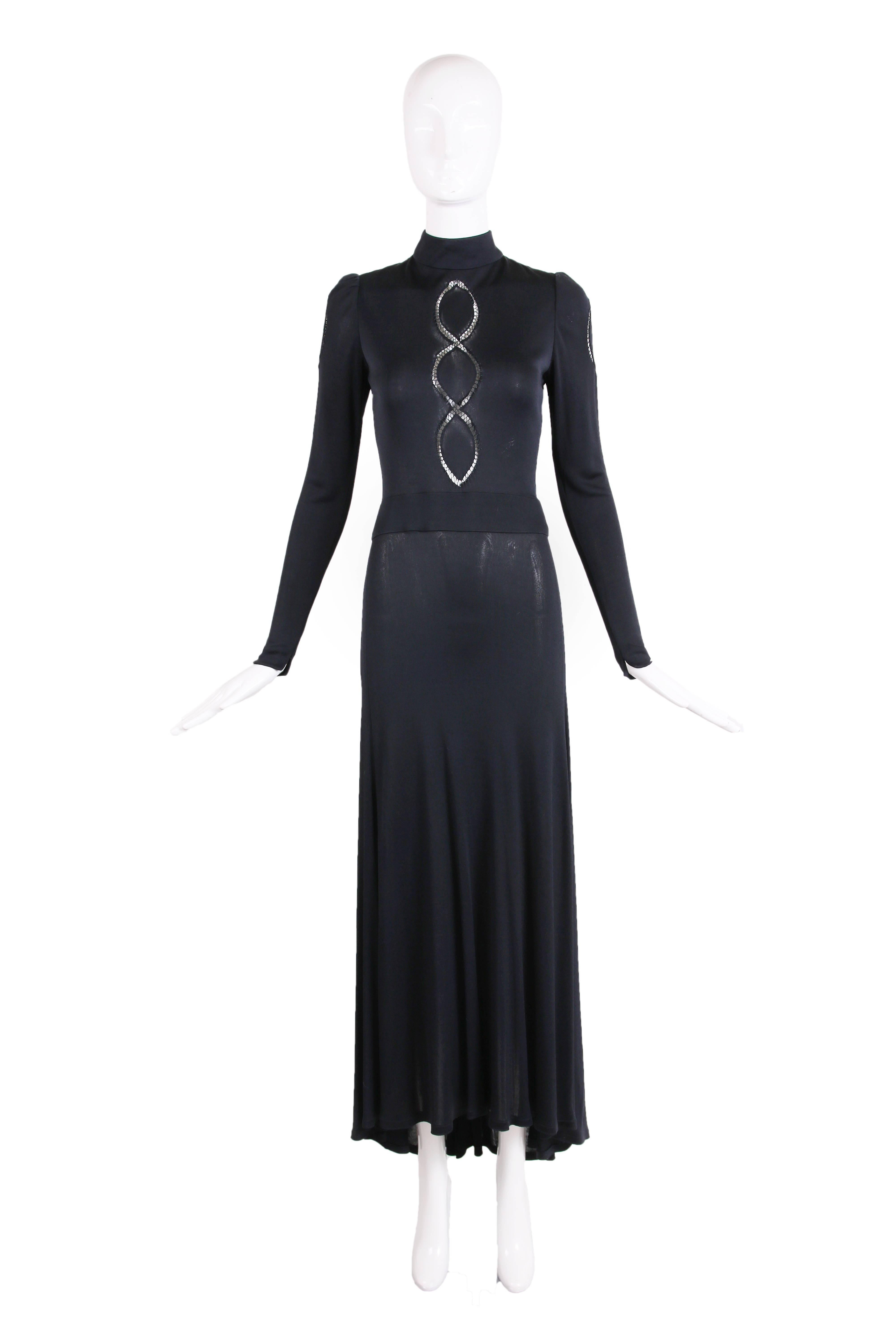 1970's Donald Brooks black jersey long sleeve mock neck maxi dress featuring three oval cut outs with threaded detail down center front and at each upper arm sleeve. The sleeves have a slit at each cuff. There is a thick waist band at the drop