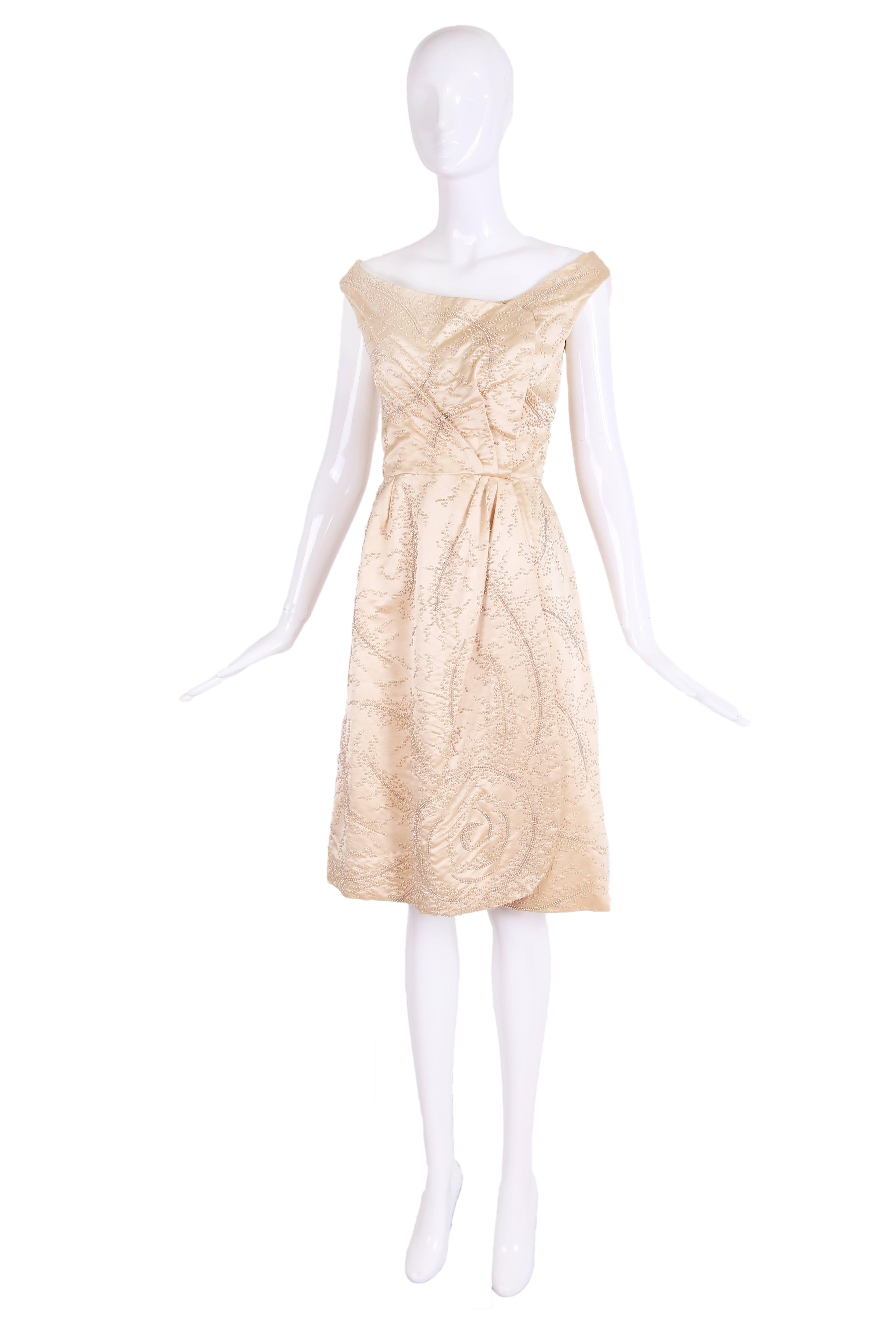 Ca. 1965 Ceil Chapman champagne-colored satin faux pearl beaded cocktail dress. Dress features an A-line silhouette with a mock wrap at front and zipper closure at back.  The dress itself is in excellent condition however there is scattered bead