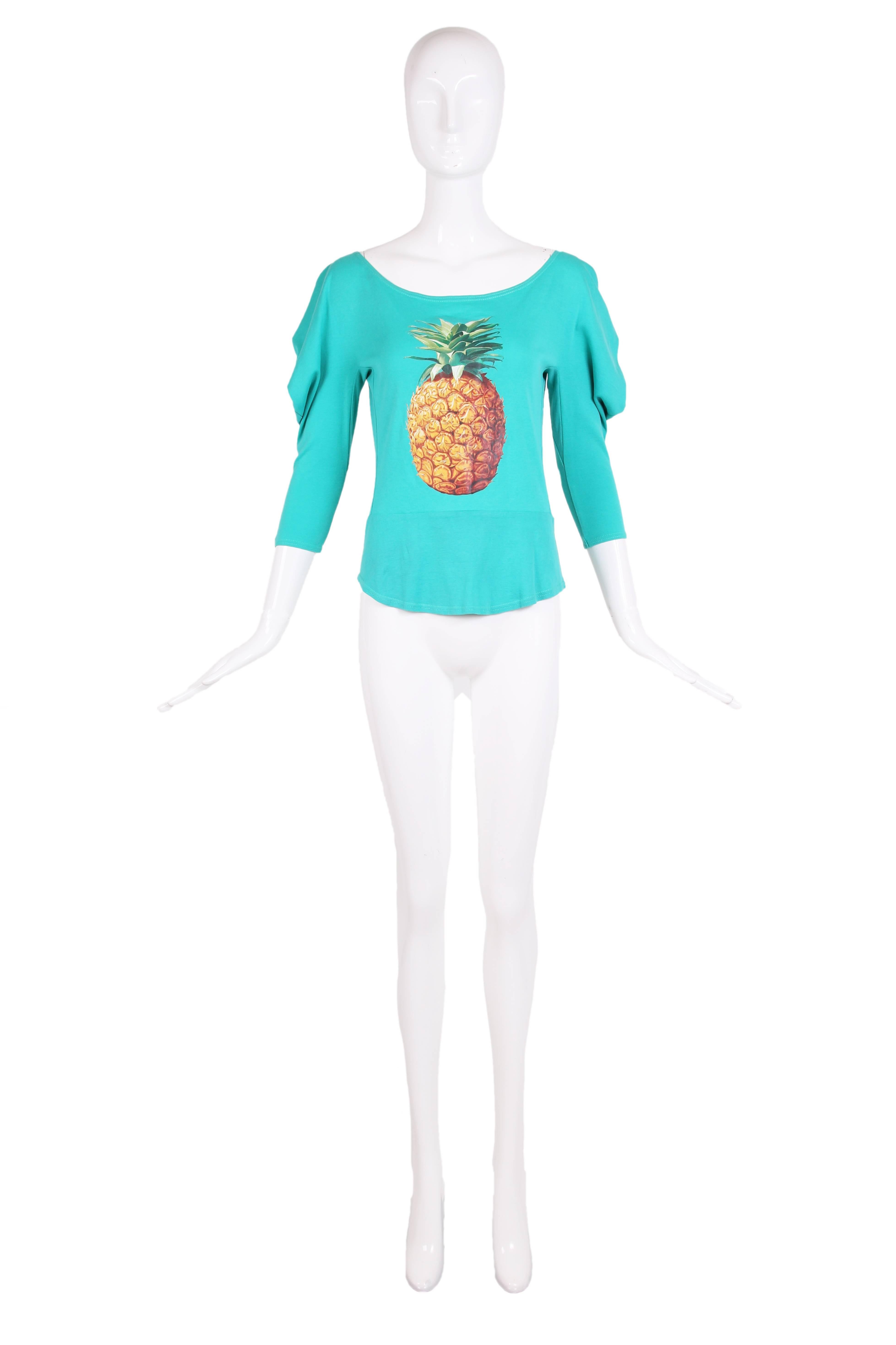 Iconic Chloe by Stella McCartney green cotton long-sleeved T-shirt featuring a pineapple graphic. The T-shirt has a boat neckline and soft shoulders that drape into a cowl detail. There is a form-fitting peplum below the waist. In excellent
