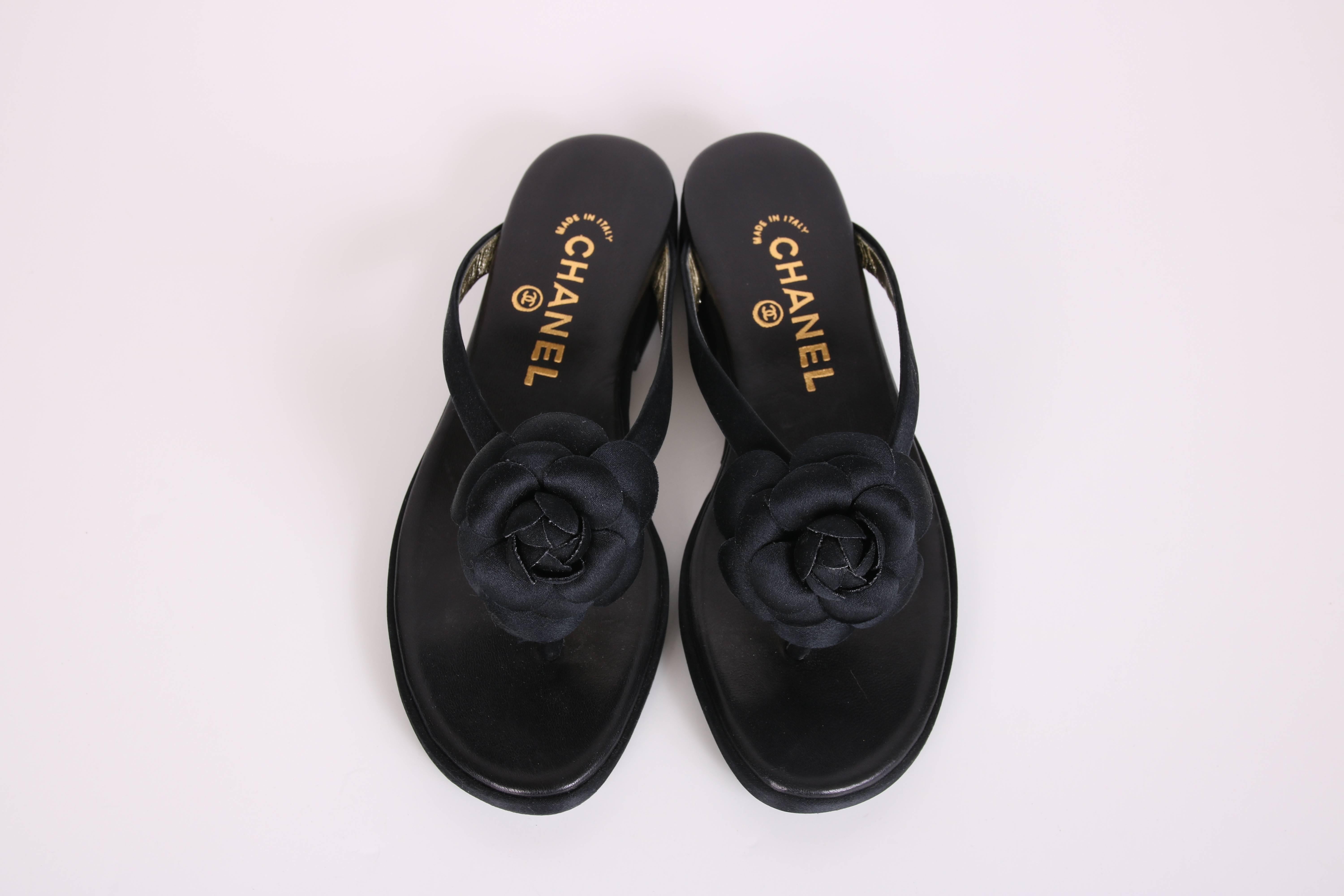 Never been worn, 1998 Chanel sandals in black satin with a black satin petaled camellia at each toe. The footpad is fabricated from black butter soft leather. Size 36.5. In excellent condition. Comes with original box and dust bag for each shoe.