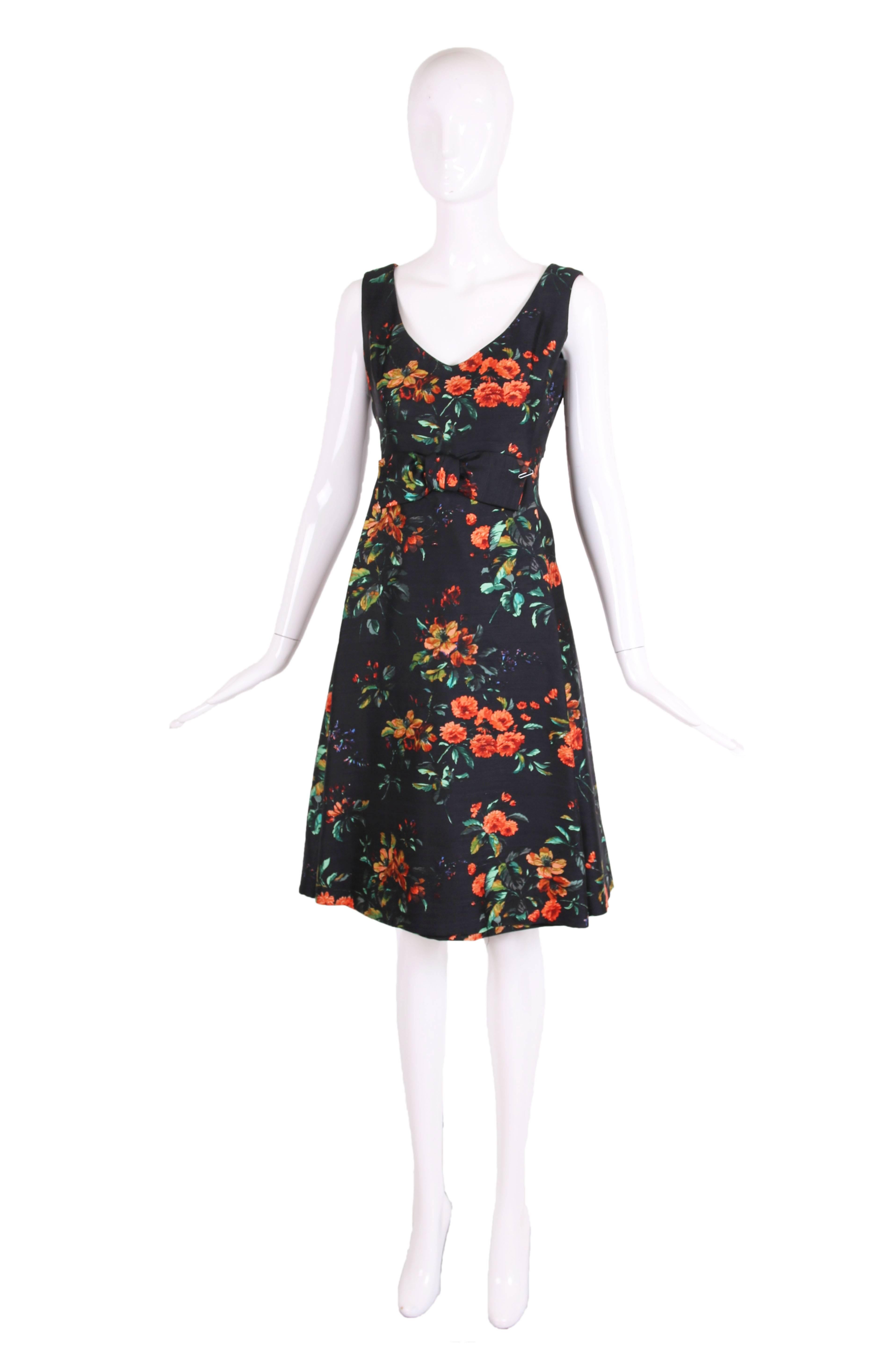1960's Christian Dior navy blue silk shantung v-neck sleeveless dress in vibrant orange and green floral pattern. The dress features a tubular front panel, cropped back panel overlay, and frontal bow at the waist. In excellent condition. No size