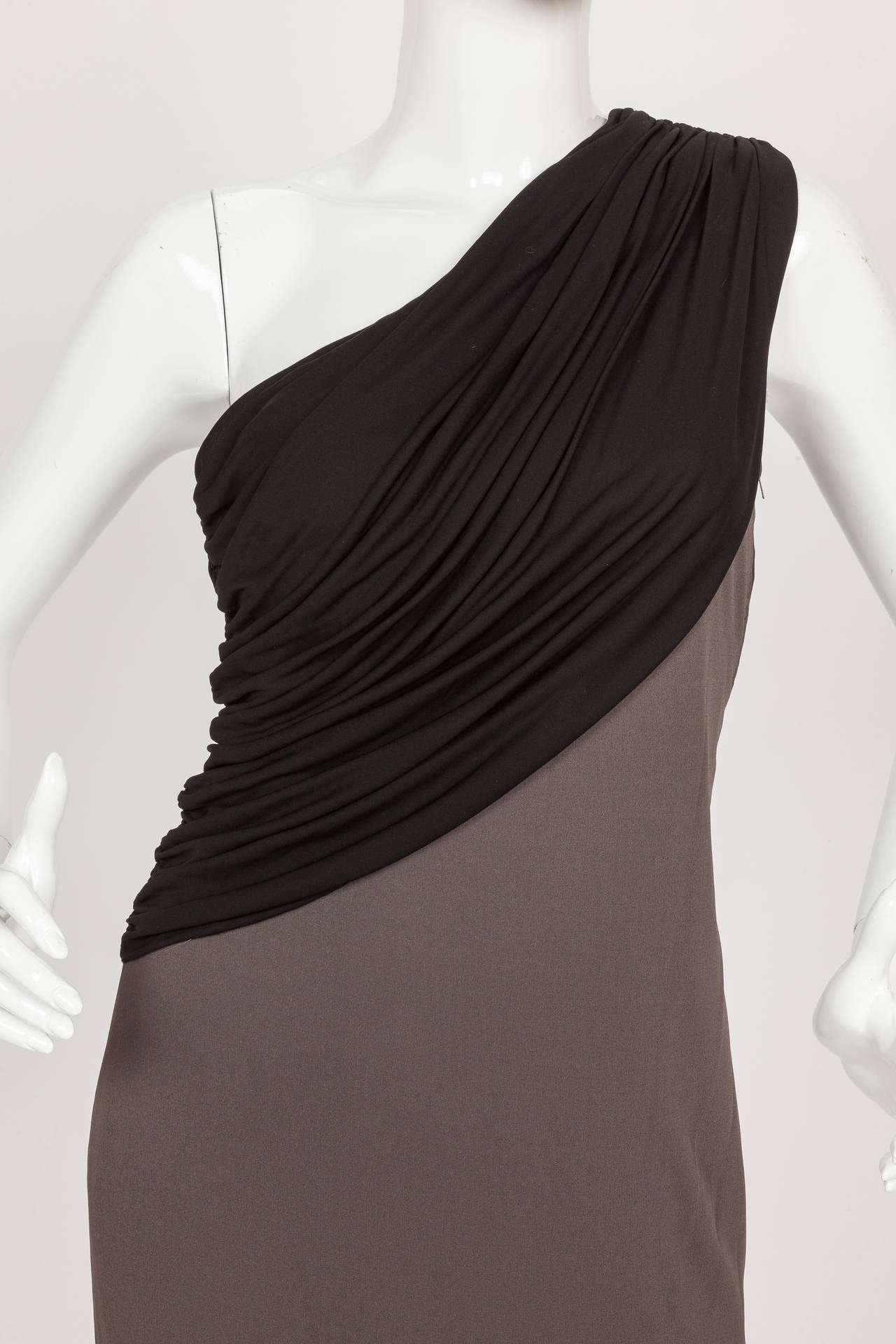 A circa 1970's Madame Gres knee-length one shoulder dress in shades of black and slate grey silk jersey. The bodice is constructed from a layer of black pleated and draped silk jersey and the dress is lined at the interior with silk. Hidden zipper
