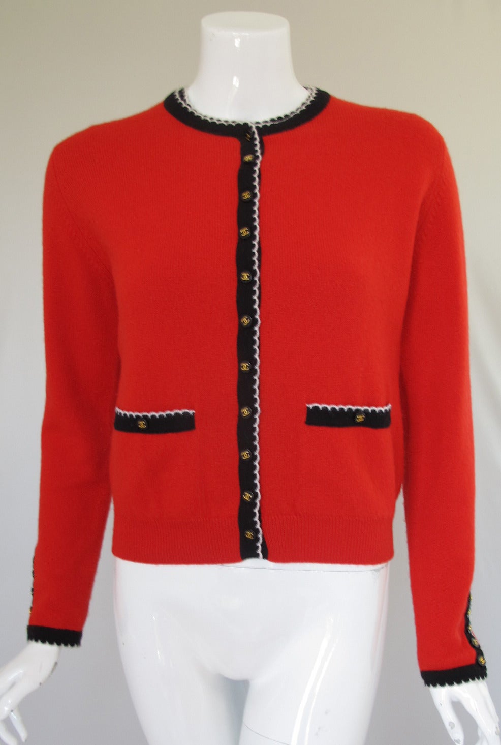 Chanel 100% cashmere twinset in red with black and white trim and black with gold Chanel CC logo buttons. The sweater beneath the cardigan is short sleeved with a button at the back neck. The size tag has been removed but my guess is this will fit a