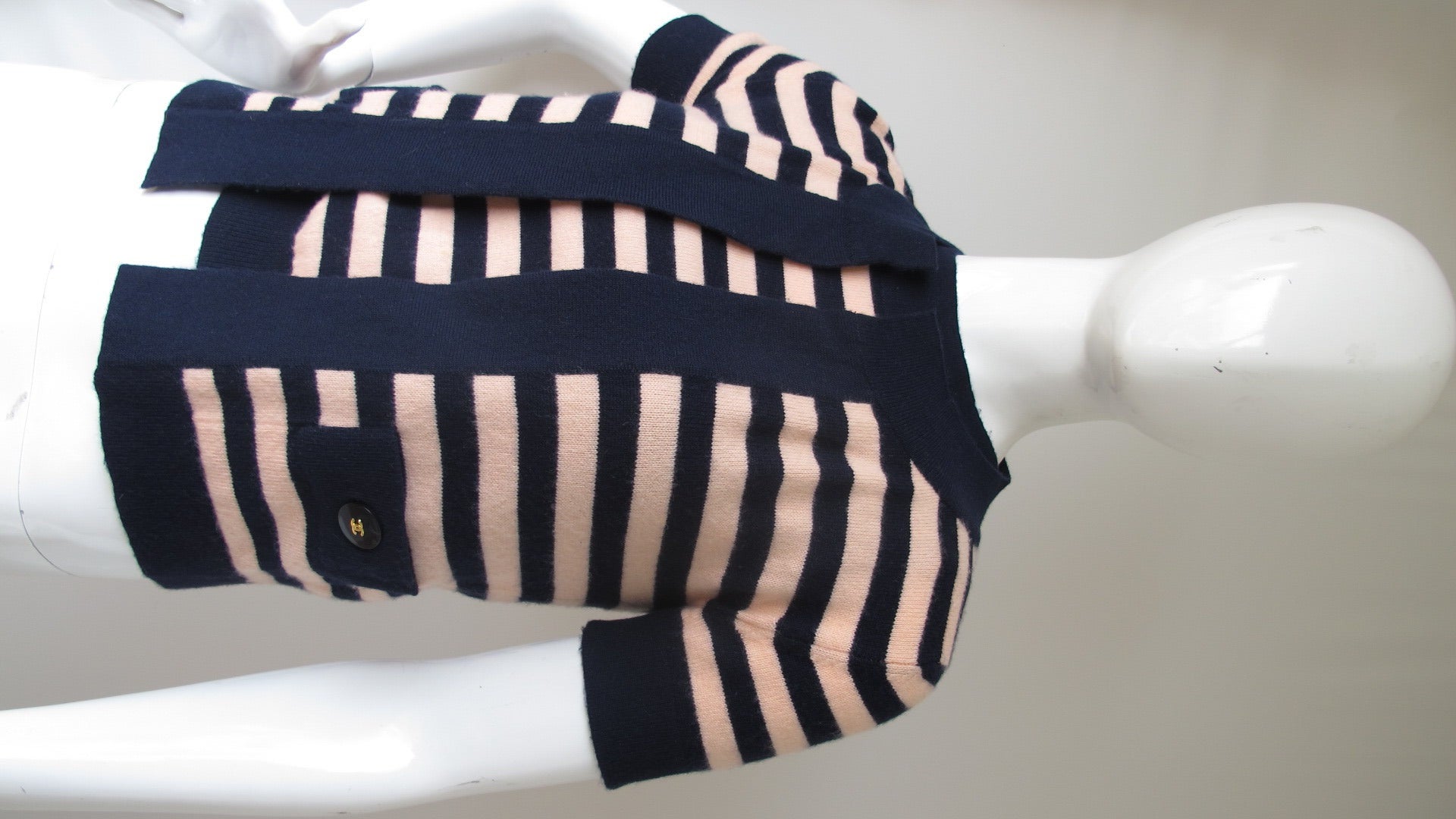 A 1997C Chanel 100% cashmere navy blue and pink striped short-sleeved twinset trimmed with bands of two-inch navy cashmere. The cardigan is open with two front pockets featuring gold on black CC logo buttons and the sleeveless sweater underneath