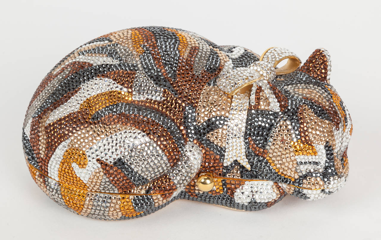 Iconic Judith Leiber minaudière in the form of a bejeweled sleeping cat with a bow around its neck. The hard clutch is covered all over with mini Swarovski crystals in shades of brown, silver, amber, slate gray, light gray, golden orange and pale