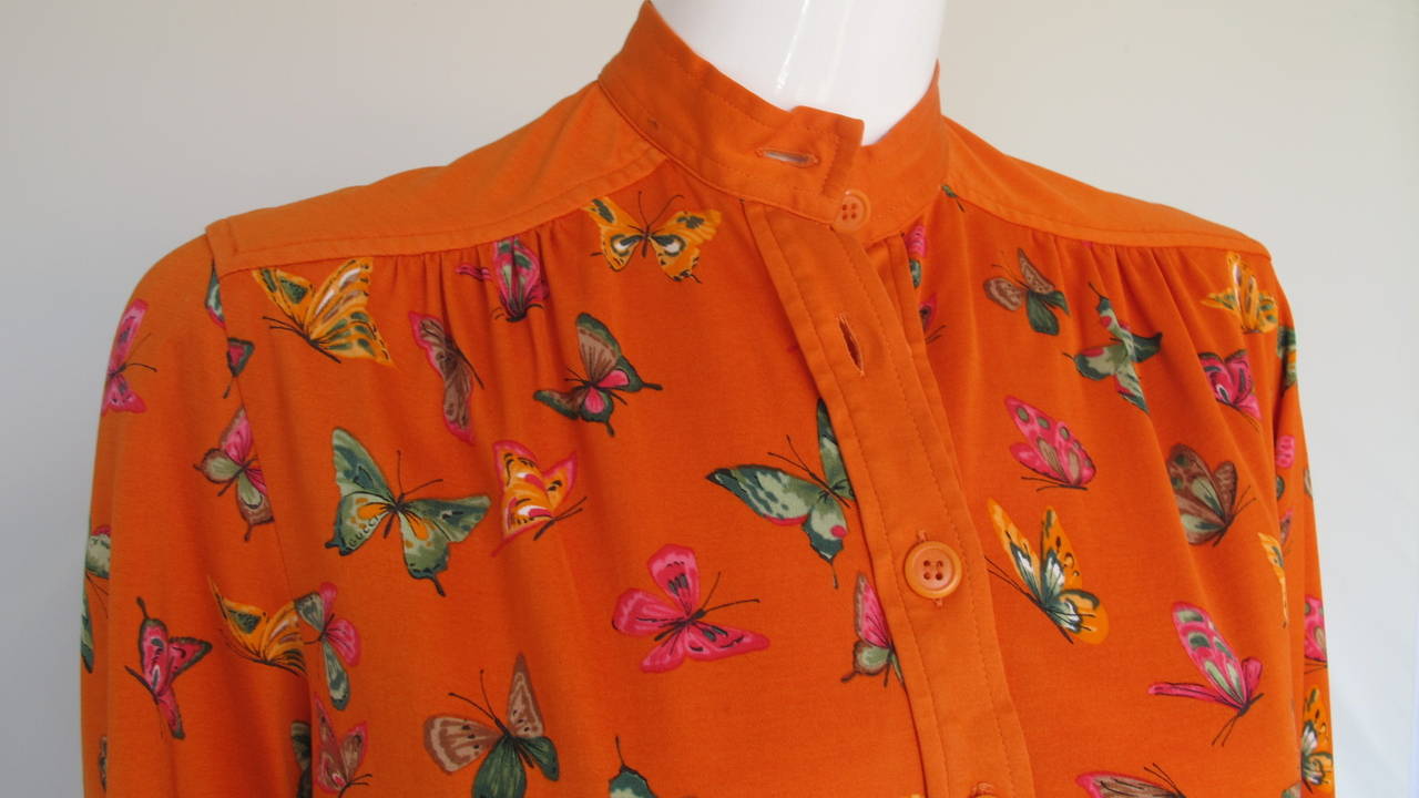 A vintage 1970s Gucci cotton shirt dress in orange with butterfly print in shades of pink, green, light orange, taupe and black. Features dual sides pockets, stand collar, button closure at bodice front and cuffs as well as solid polished cotton