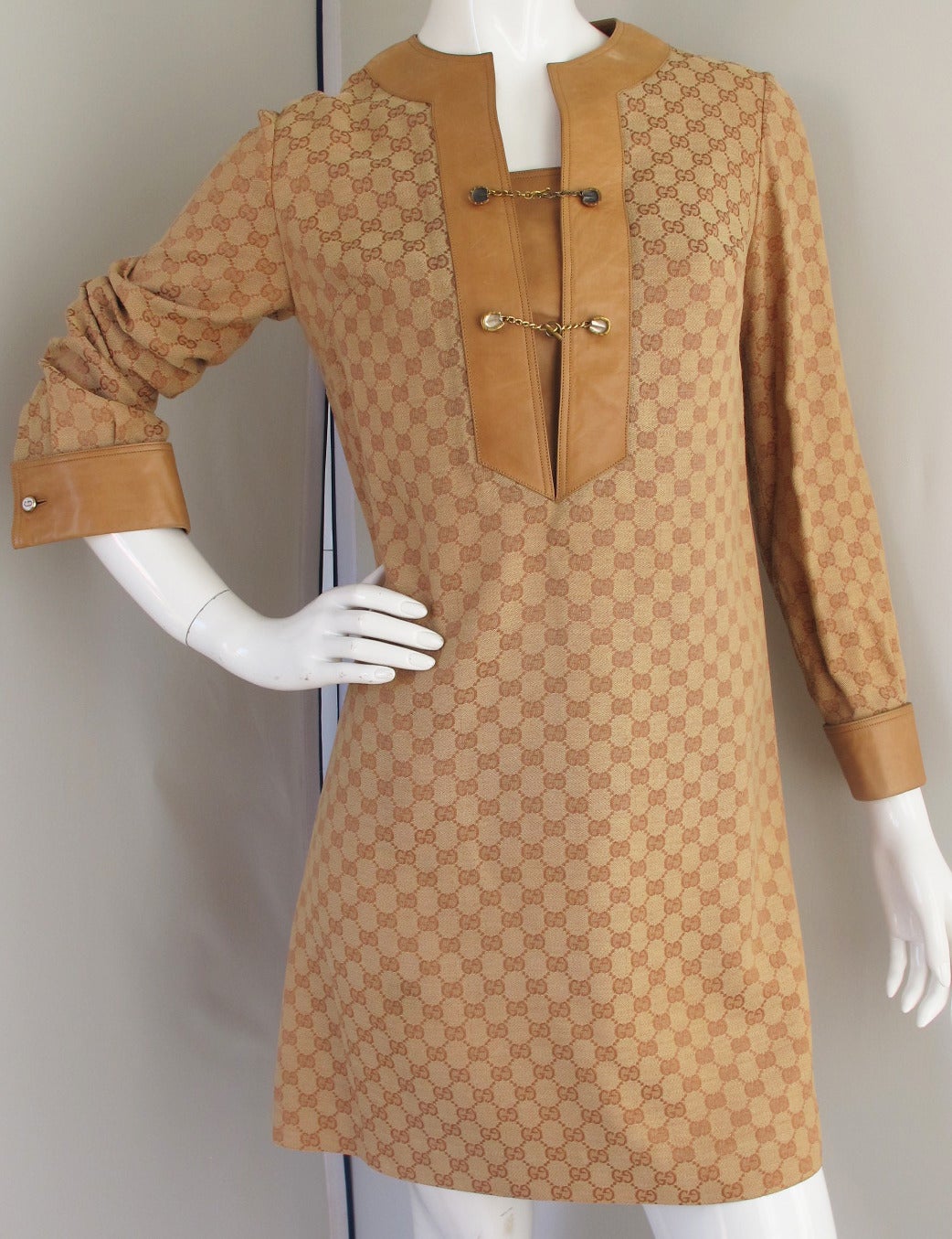 1970s Gucci monogrammed canvas tunic dress in a camel color with light brown GG logo. Trimmed with leather and fastening at the chest with gilt horse hoof hardware (stamped Gucci 800) and 