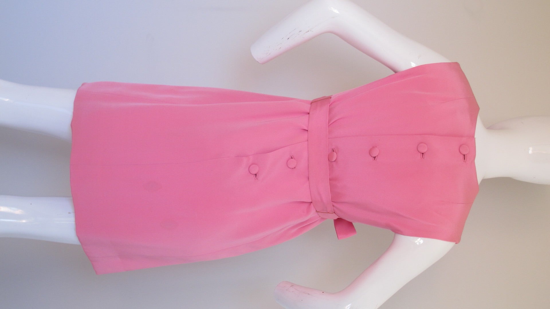 A 1960's Donald Brooks pink silk sleeveless shift dress that could be worn during the day or for cocktail hour. Silk button closure at the back, tie waist and pink silk lining. In good condition with some almost imperceptible fading at the shoulder