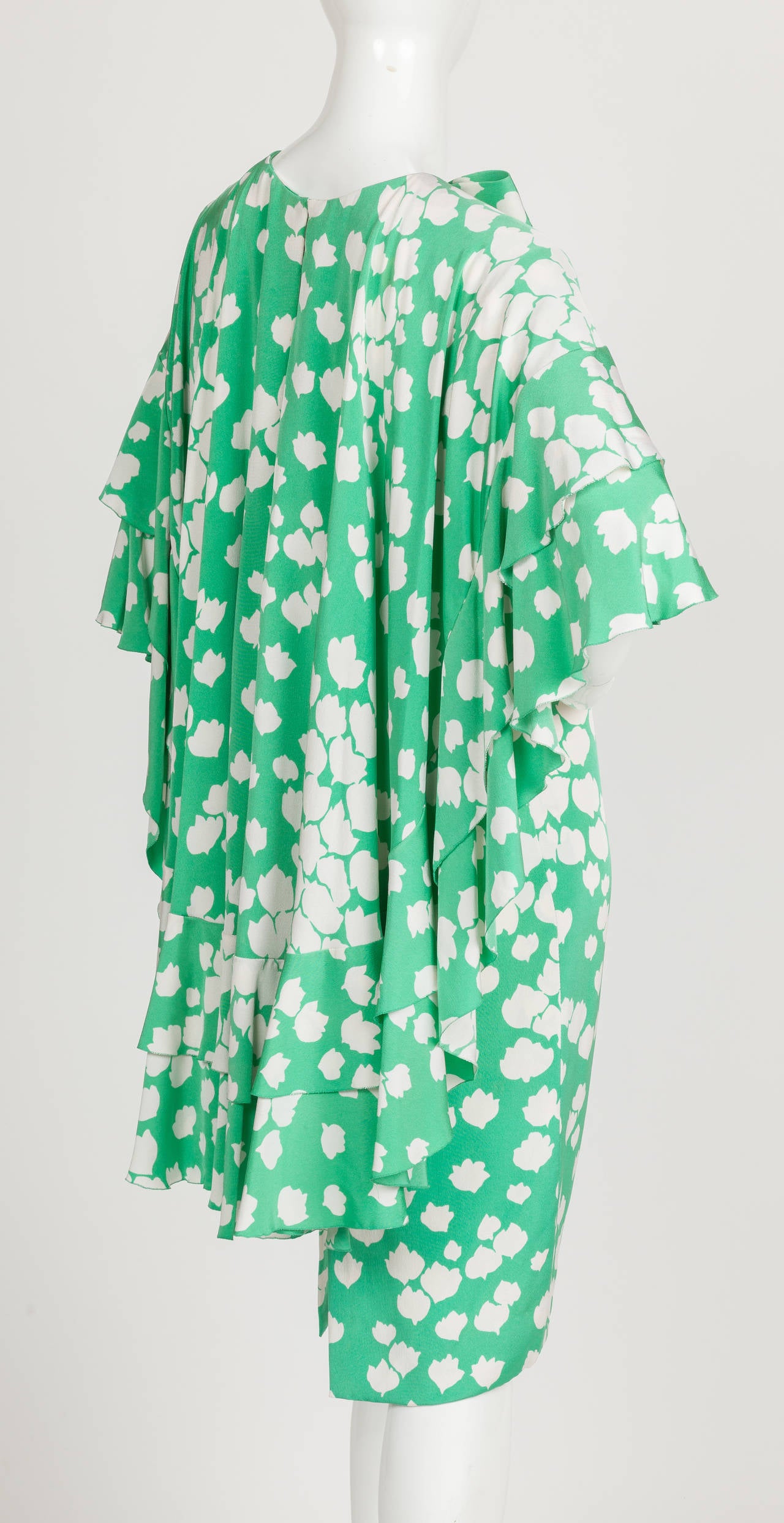 A Pierre Cardin attributed green and white silk tea length shift dress with abstract flower print. The standout element of this dress is the ruffled cape that attaches at the shoulders and cascades down the back and is completed by a decorative bow