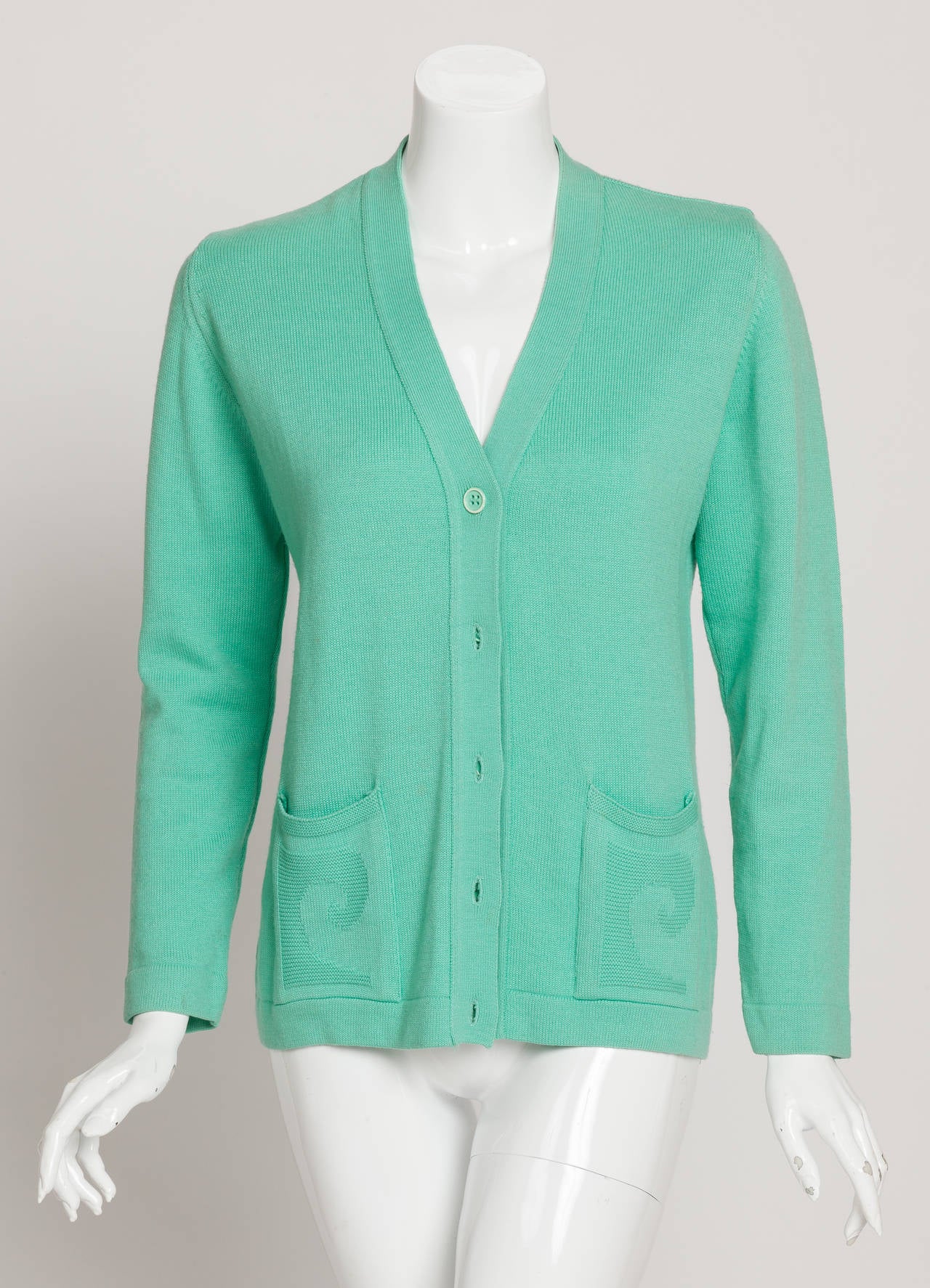 A vintage Pierre Cardin aqua green v-neck cardigan sweater with raised logo pockets. The cardigan buttons up the front and has two side front pockets decorated with a raised knitted Cardin logo design. In excellent condition with some wear to the