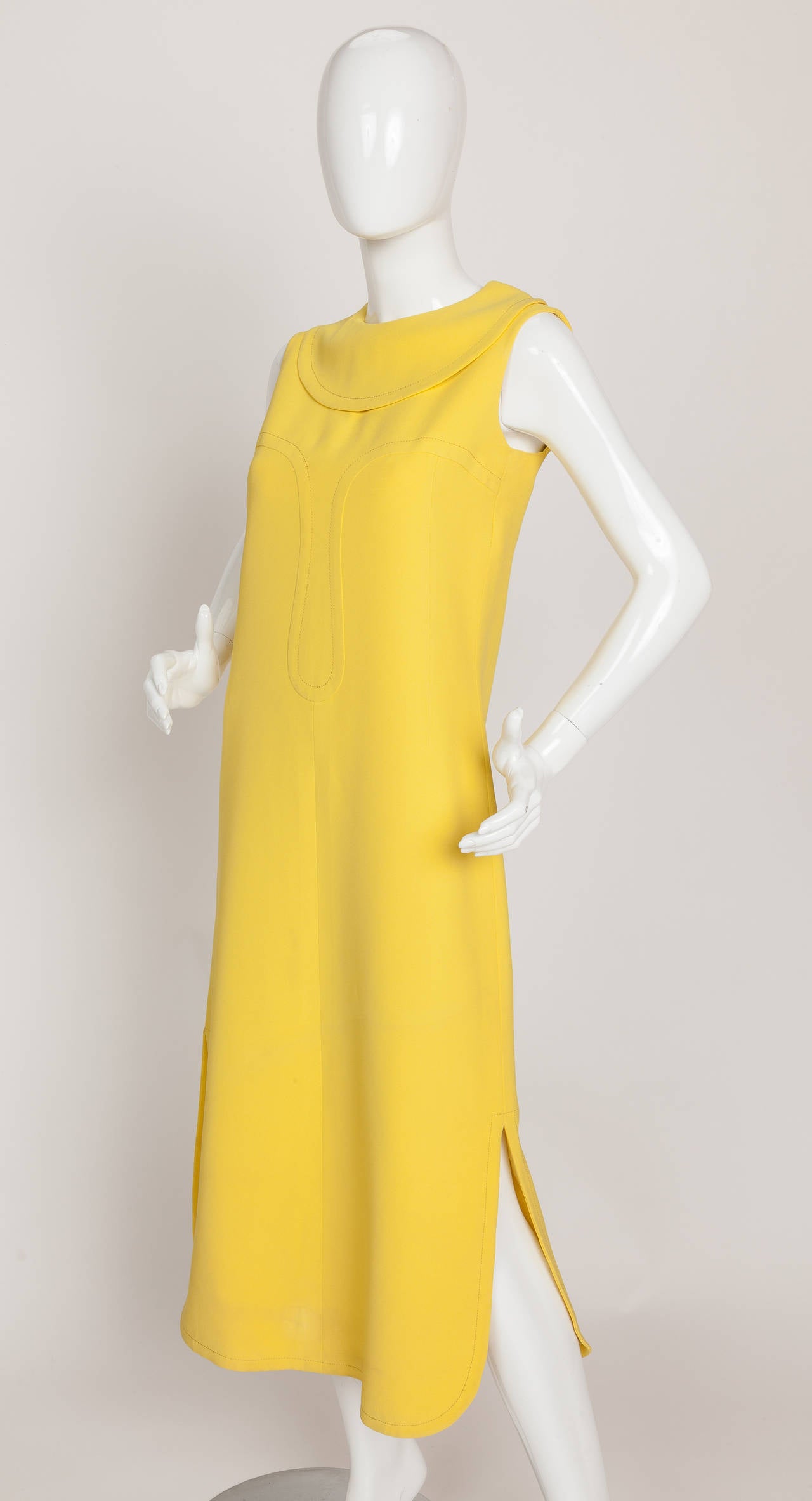 A Pierre Cardin attributed sunshine yellow chasuble dress with rounded slits on either side of the hem and rounded foldover collar. Features tell-tale Cardin design elements such as the topstitched geometric shape adorning the center front and top