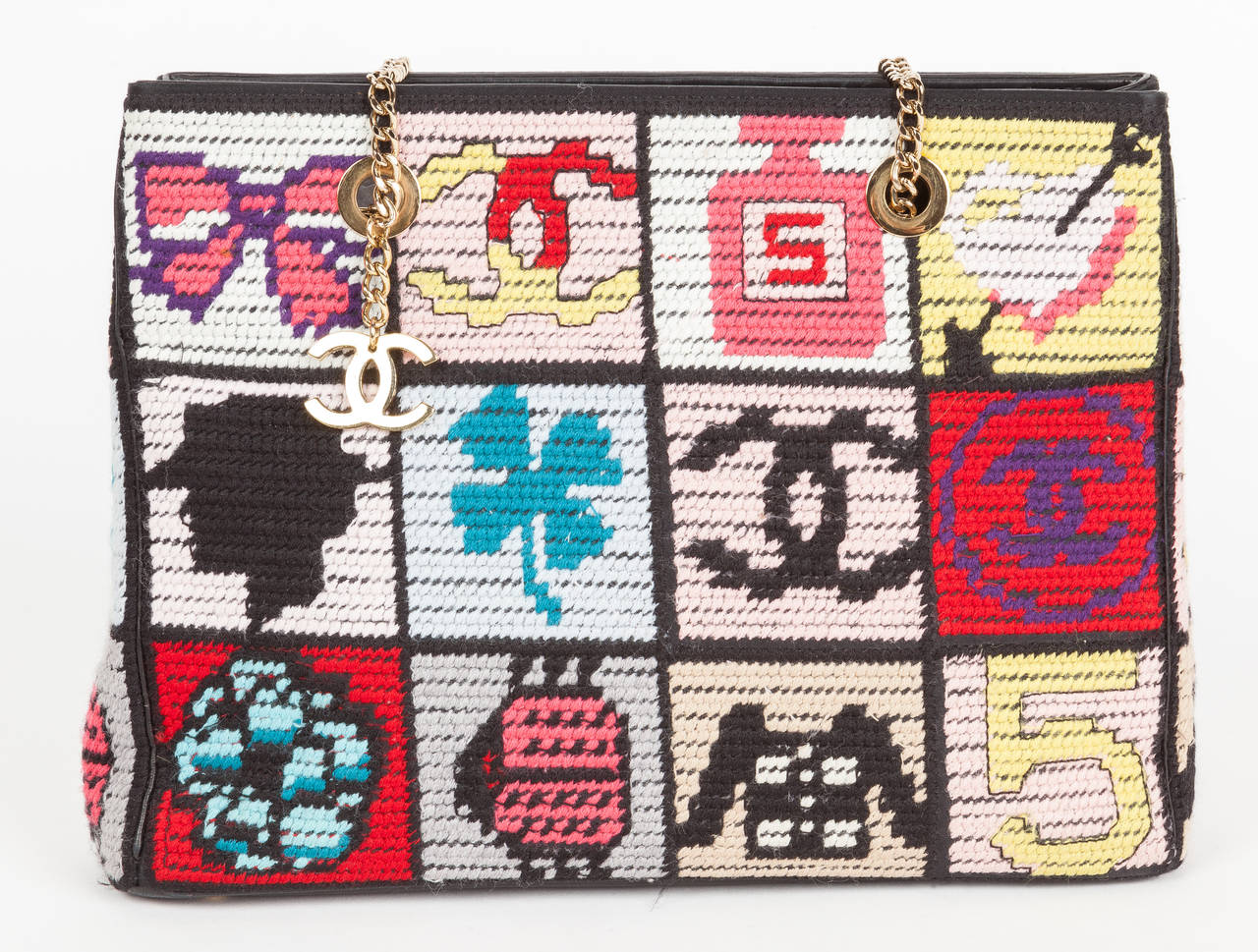 A Chanel “Precious Symbols” shoulder bag crafted from colorful needlepoint squares depicting classic and iconic Chanel symbols. The bag has gold chain link shoulder straps with a hanging gold Chanel CC charm, black leather bottom with four metal