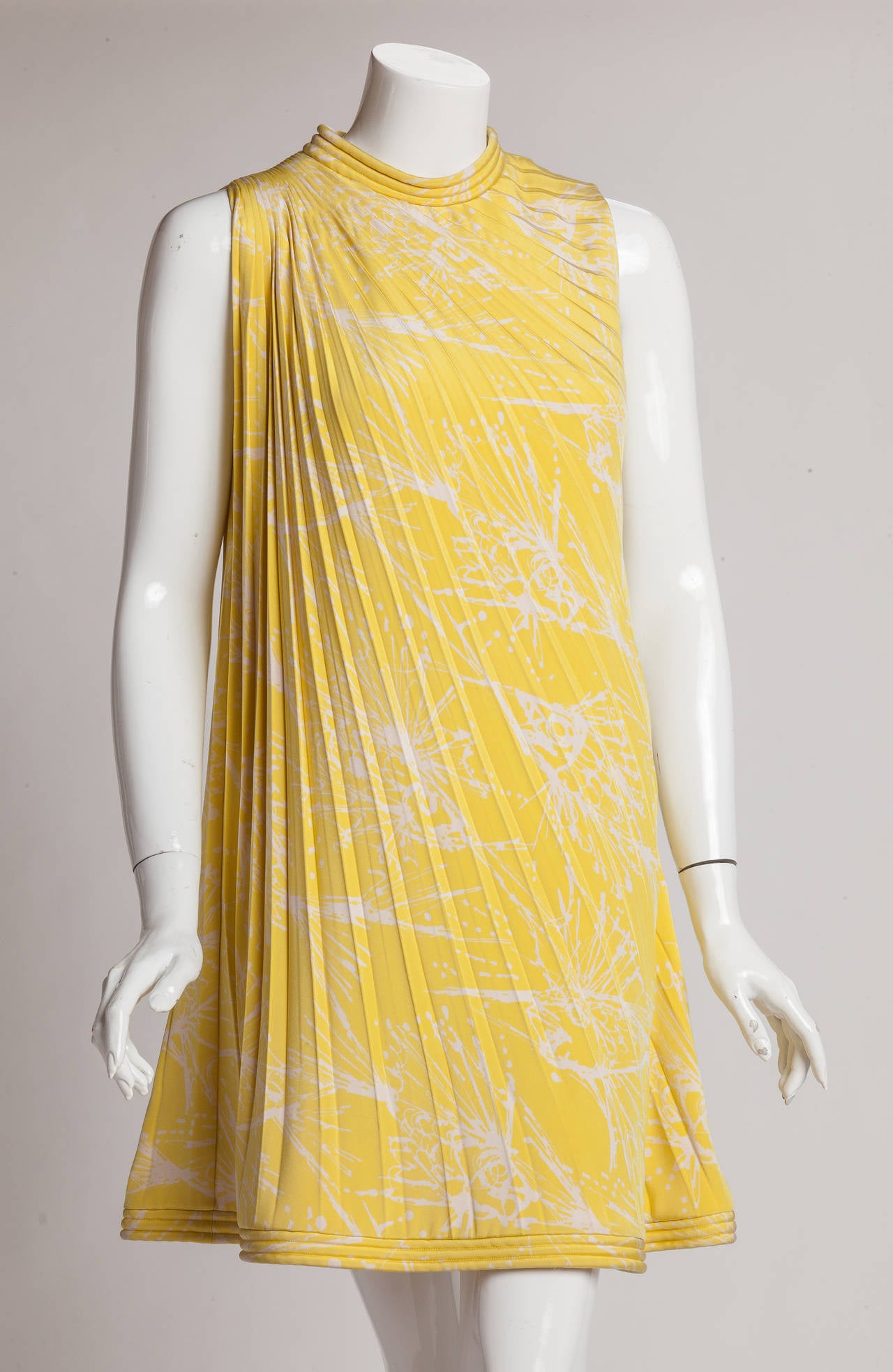 This circa 1968 Pierre Cardin haute couture shift dress is based on the concept of the spiral. Made from double-ply silk, the asymmetric pleating begins at the shoulder and fans out diagonally across the yellow and white print fabric, thereby