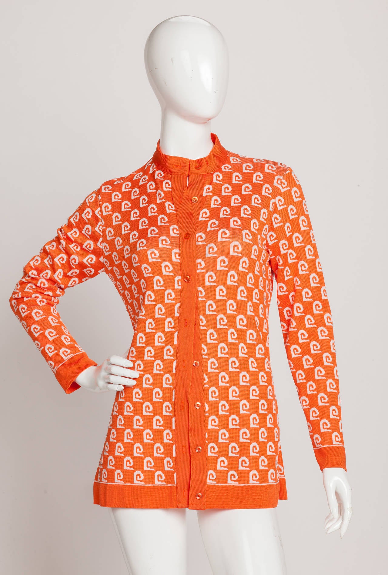 A slim fitting extra long Pierre Cardin orange logo cardigan sweater with high collar and orange trim. At one point, the Pierre Cardin logo was ubiquitous with 100's of licensing deals that branded the now-famous logo and signature not only on