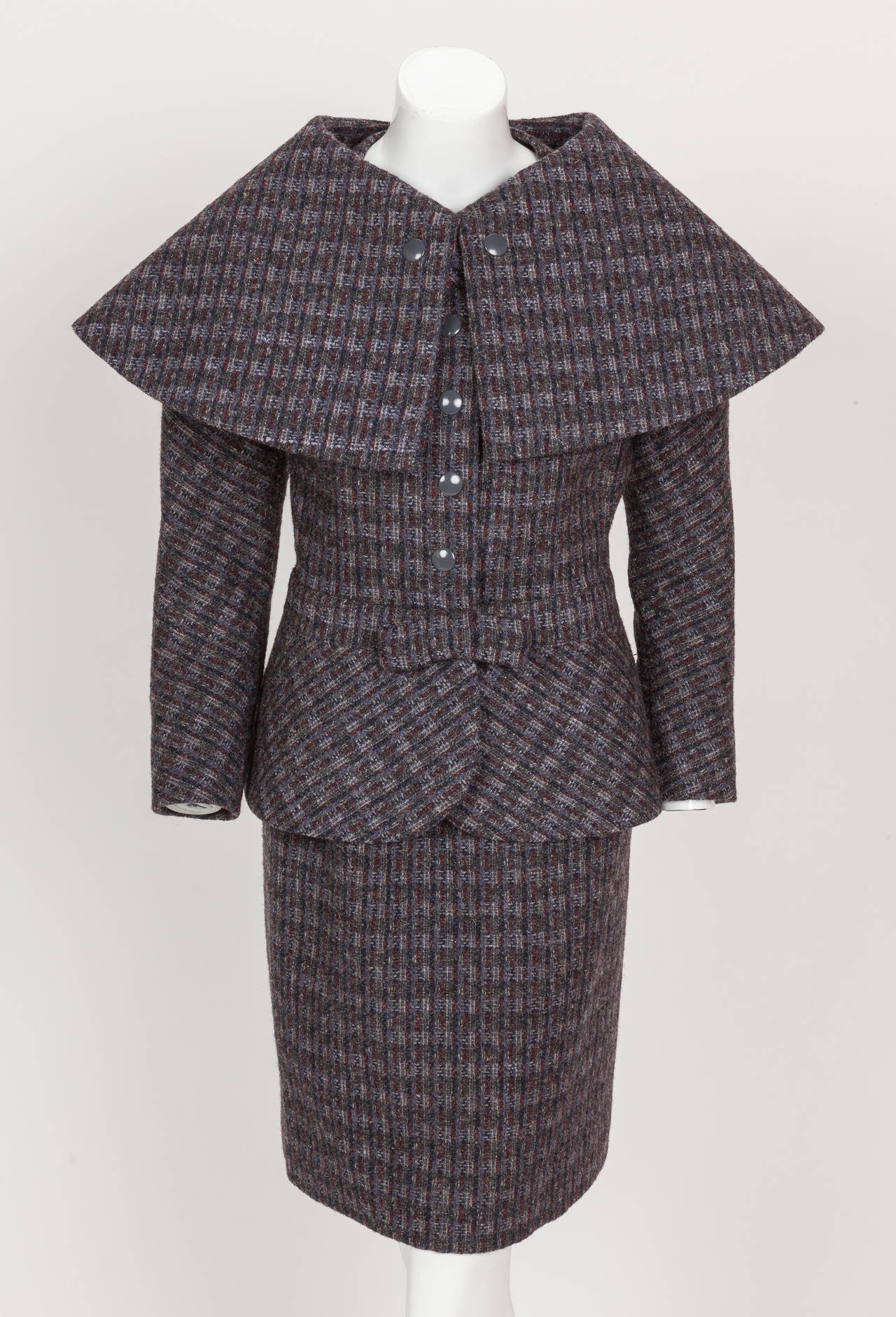 A circa 1982 Pierre Cardin jacket and skirt suit with oversized detachable shawl collar in shades of maroon, light violet and navy blue wool tweed. The button down jacket features raglan sleeves, frontal gray metal snaps and an oversize detachable