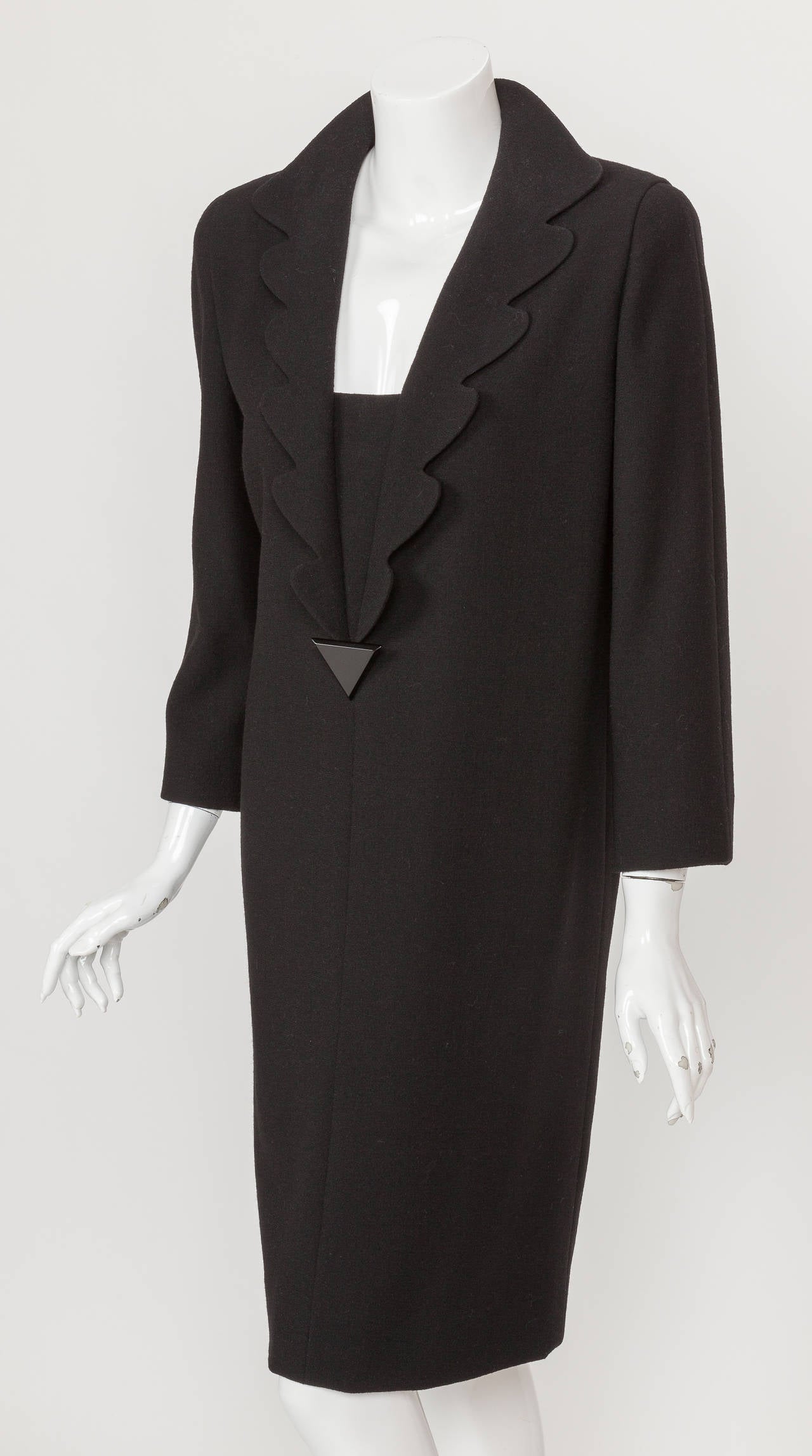 A circa 1992 Pierre Cardin haute couture black wool crepe cocktail dress. This sophisticated cocktail dress features a long petalled lapel and is ornamented with an upside down triangle-shaped black button. The silhouette features a subtly tapered