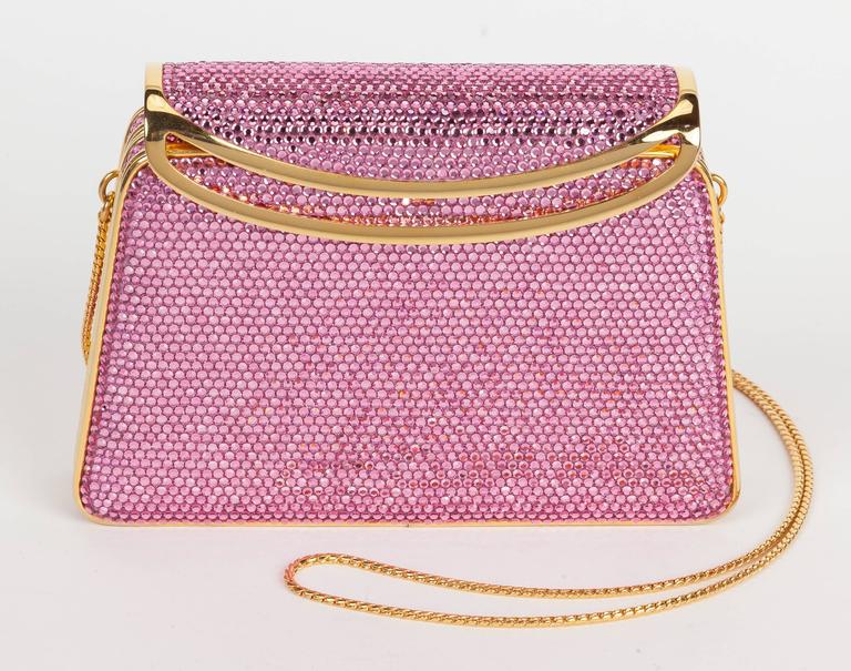 A Judith Leiber pink minaudière evening purse entirely covered with pink Swarovski crystals. Features gold tone metal trim, a hinge-top opener/clasp and gold leather lined interior. Comes with gold tone chain shoulder strap that can either be