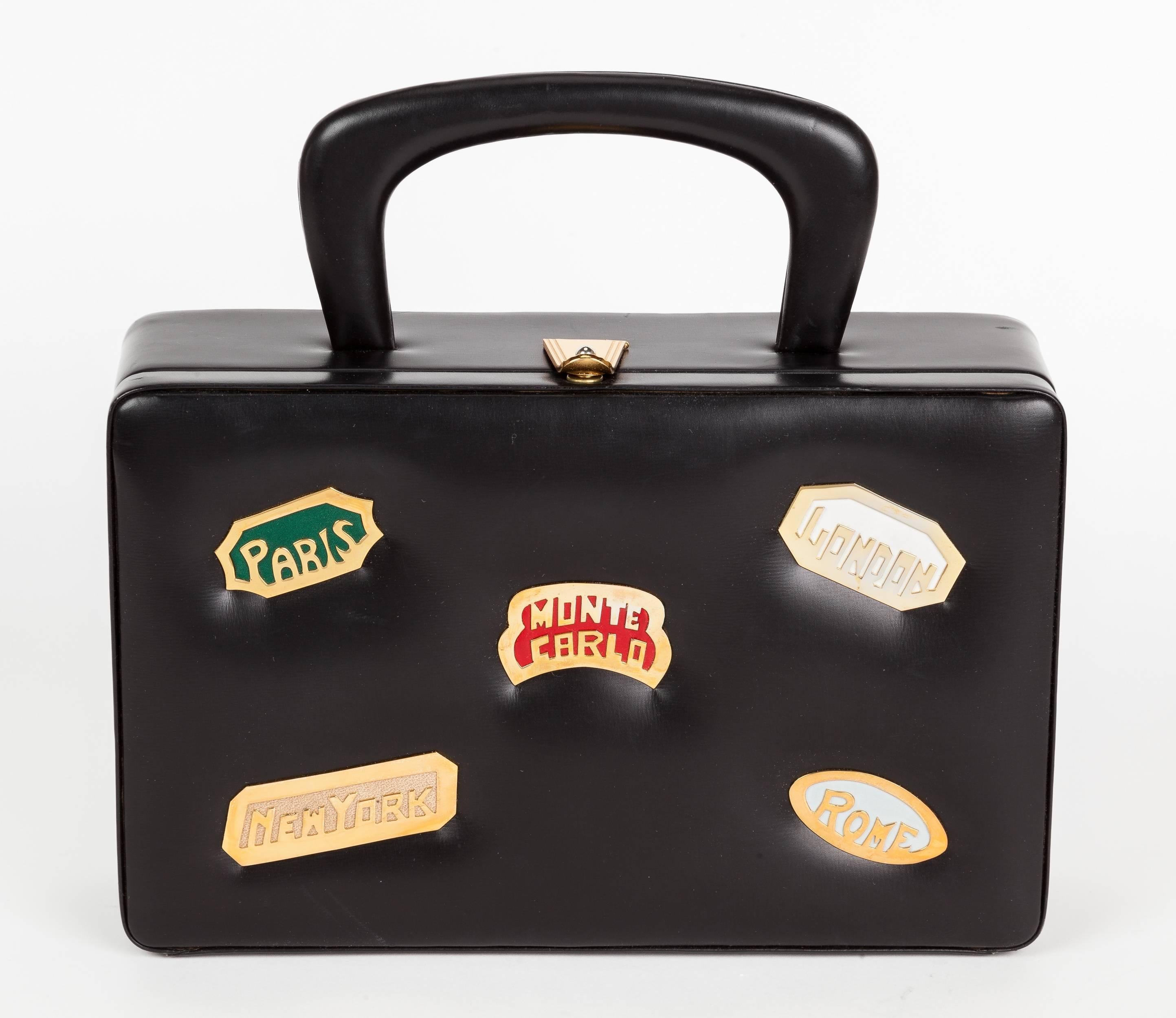 From the now-defunct New York handbag maker Prestige, is this 1960's smooth black calfskin destination bag, box purse with metal plaques bearing the names of cities: Paris, New York, Monte Carlo, London and Rome. The box purse opens via means of a