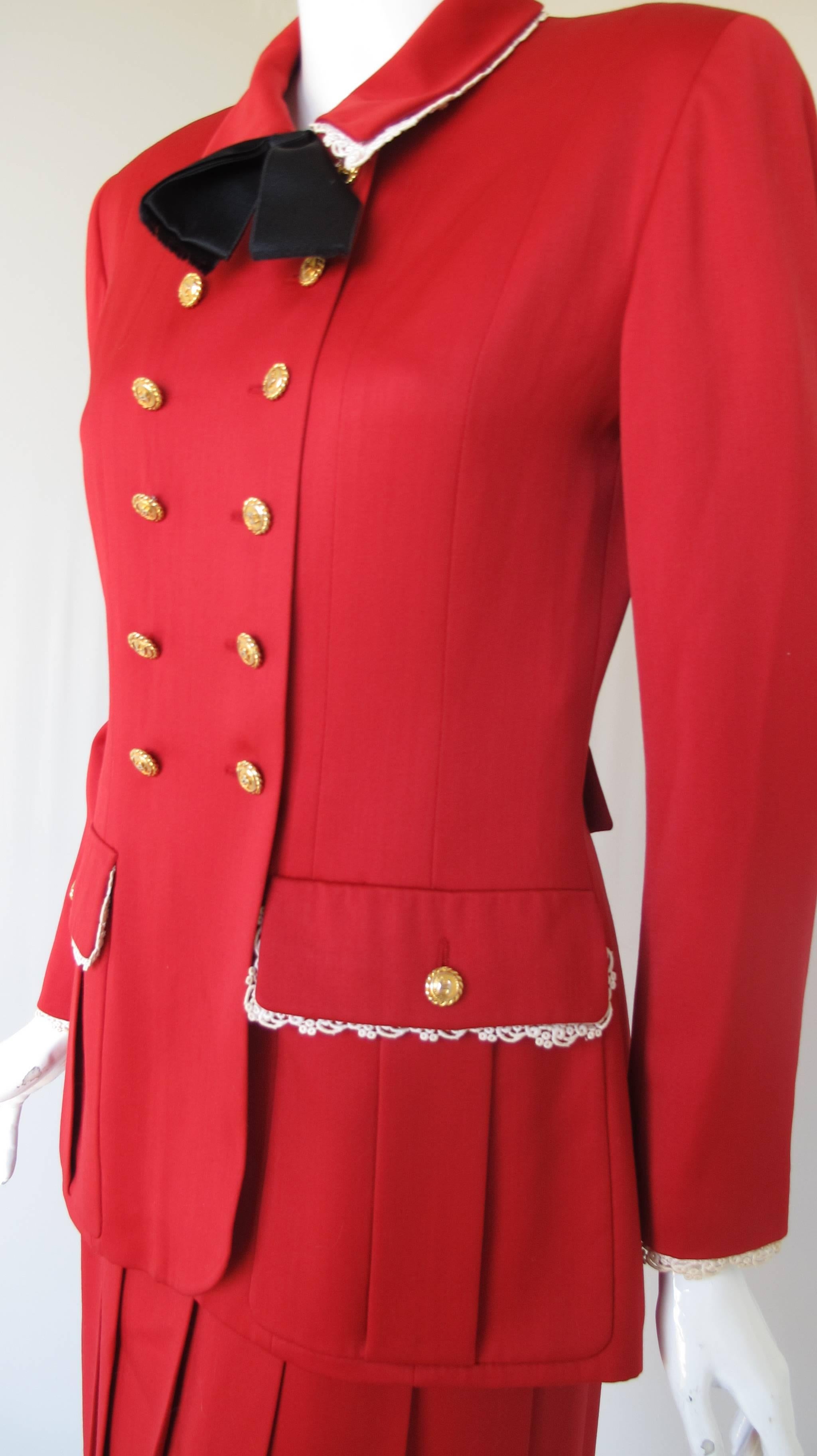 A vintage Chanel red summer wool suit comprised of a jacket and drop pleated skirt. The jacket is lined with CC logo silk and trimmed with lace at the collar, cuffs and frontal pockets. Features a silk bow at the neckline and CC logo gold tone