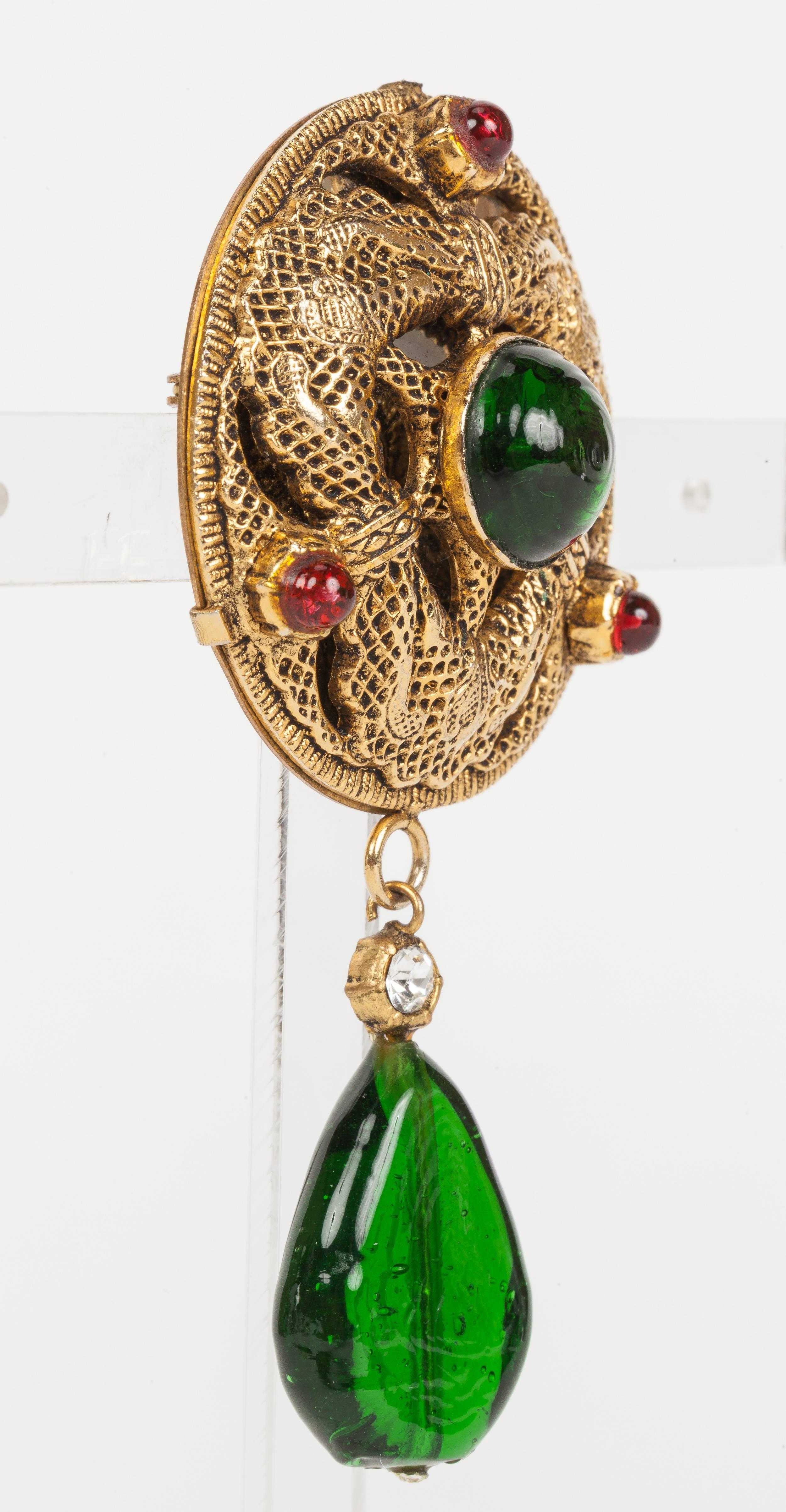A rare 1984 Chanel round mirrored brooch/pendant in gold tone textured metal embellished with red and green gripoix glass cabochons and crystals. Equipped with hook at the back that can attach to a chain. In excellent