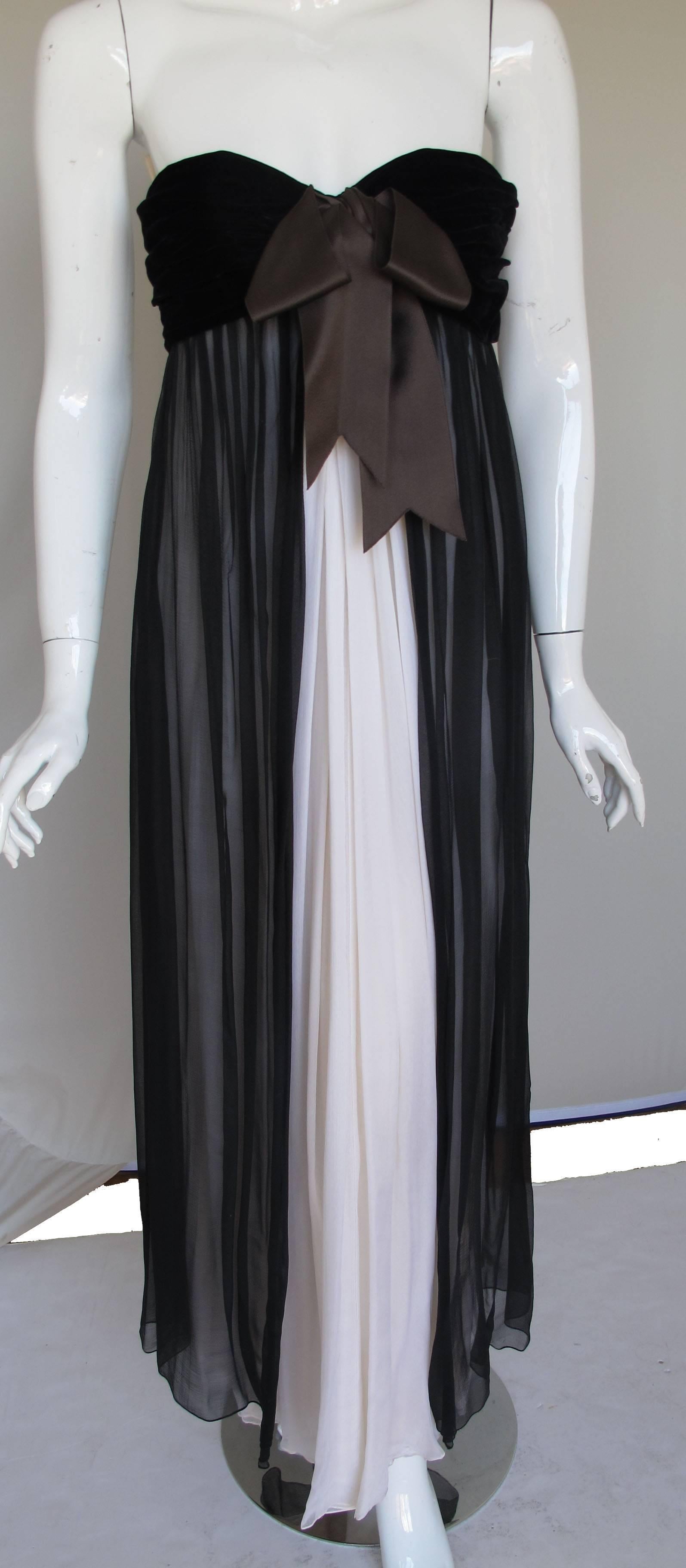 A breathtaking late 1985 Yves Saint Laurent haute couture empire style evening gown featuring a ruched black velvet top with an oversized brown silk bow and a skirt comprised of a single layer of black chiffon on top of a double layer of