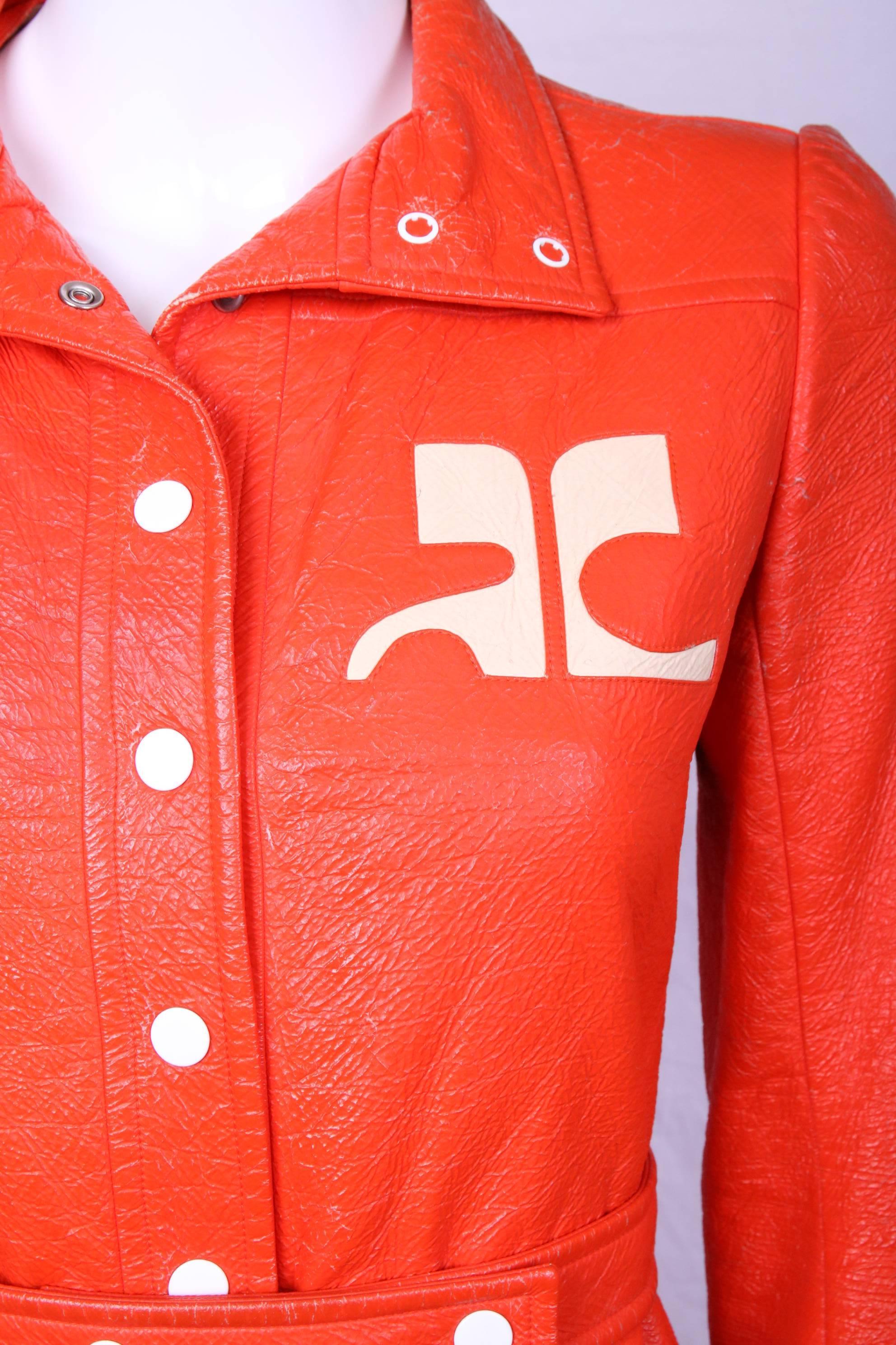 Iconic Courreges orange vinyl overcoat with zippered frontal pockets, white buttons and CC logo. Lined at the interior with Courreges logo print fabric. Size tag 