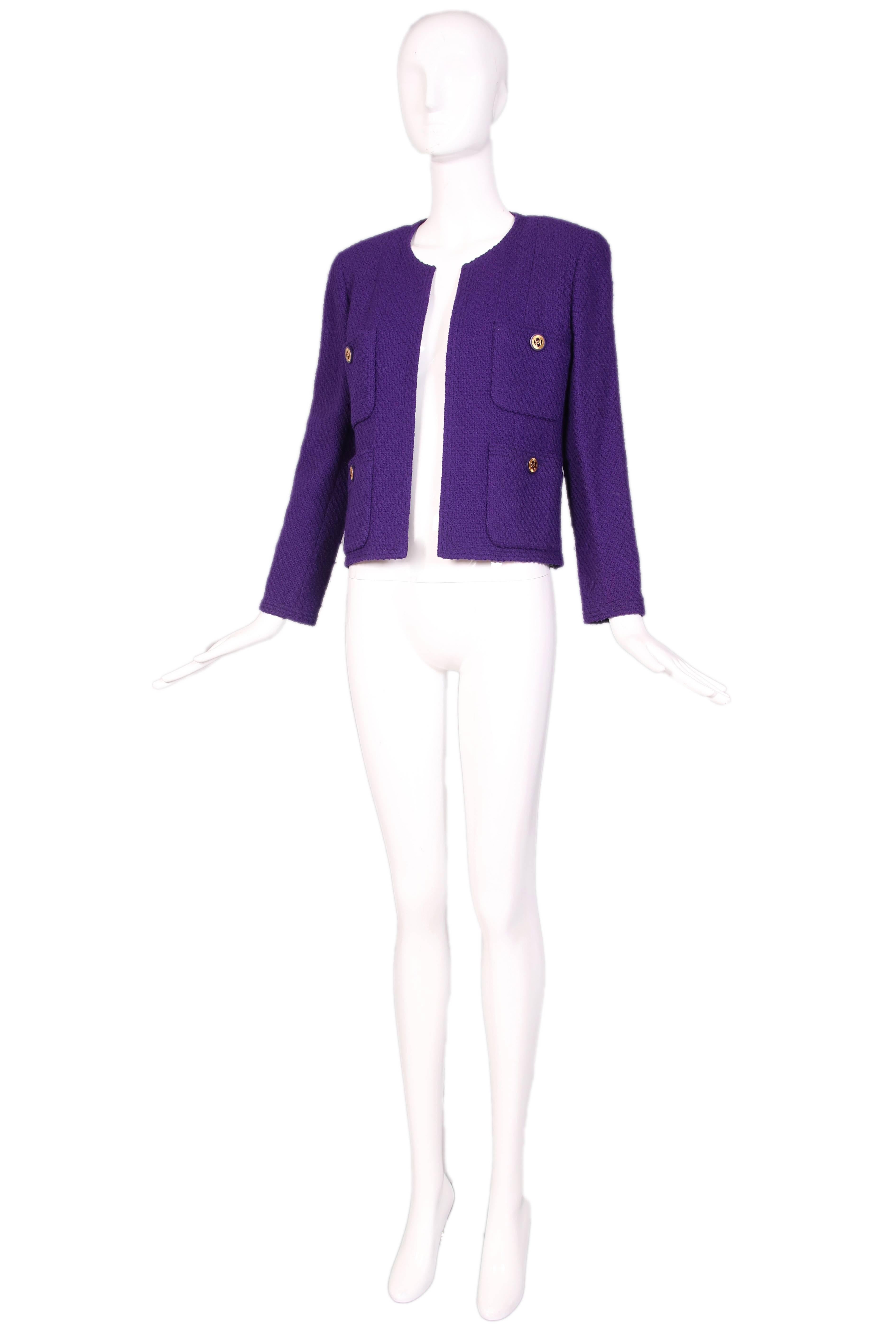 Chanel purple boucle wool open jacket featuring four pockets with Chanel logo buttons and interior lined with bejeweled winged clock print fabric. Jacket comes with dropped waist skirt that features both frontal and back overlay panels. Both labeled