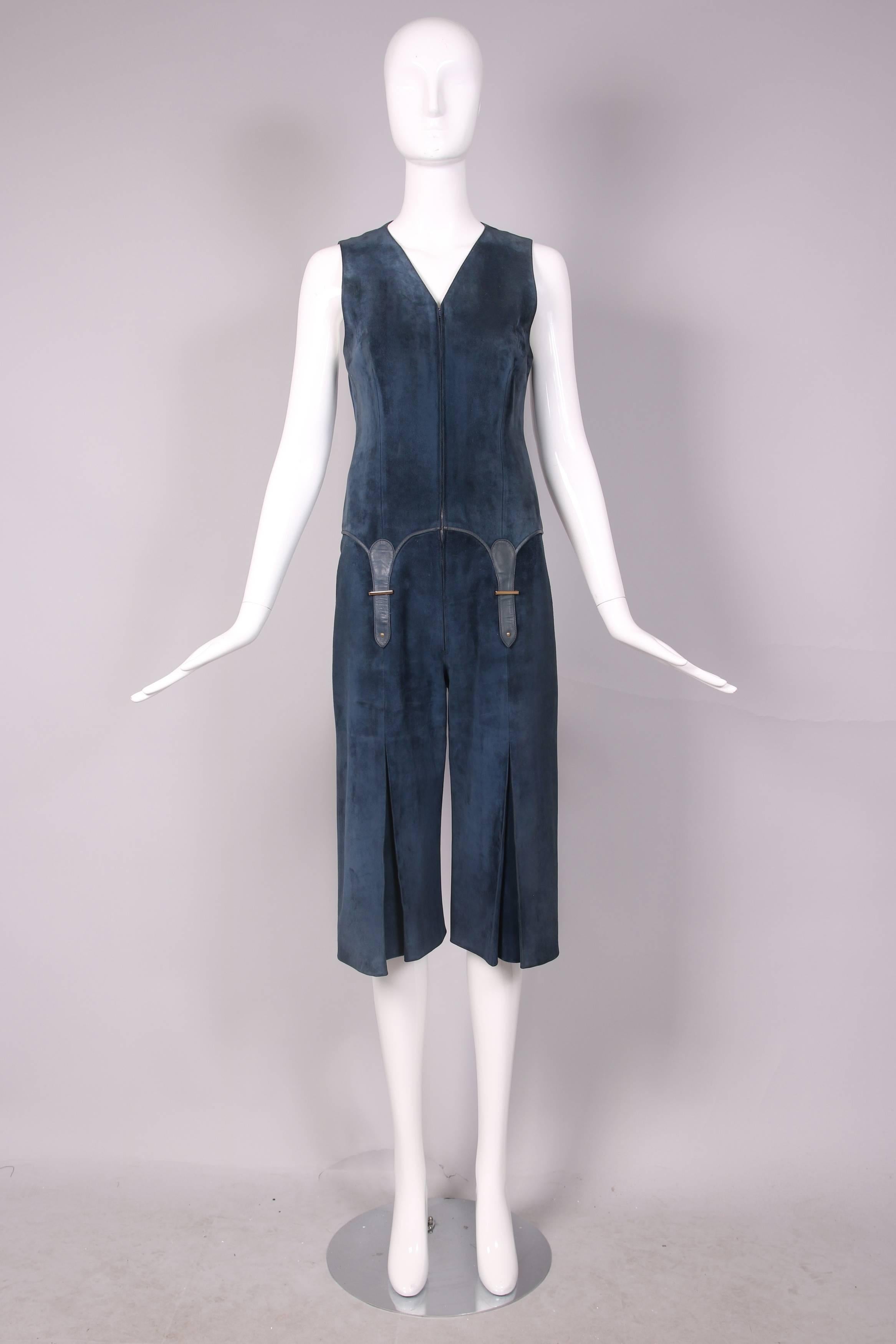 1970’s Gucci navy blue suede sleeveless jumpsuit that hits at the knee and features frontal decorative buckles as well as a kick pleat at the bottom front of each leg. Entirely lined in Gucci logo silk fabric. In excellent condition.