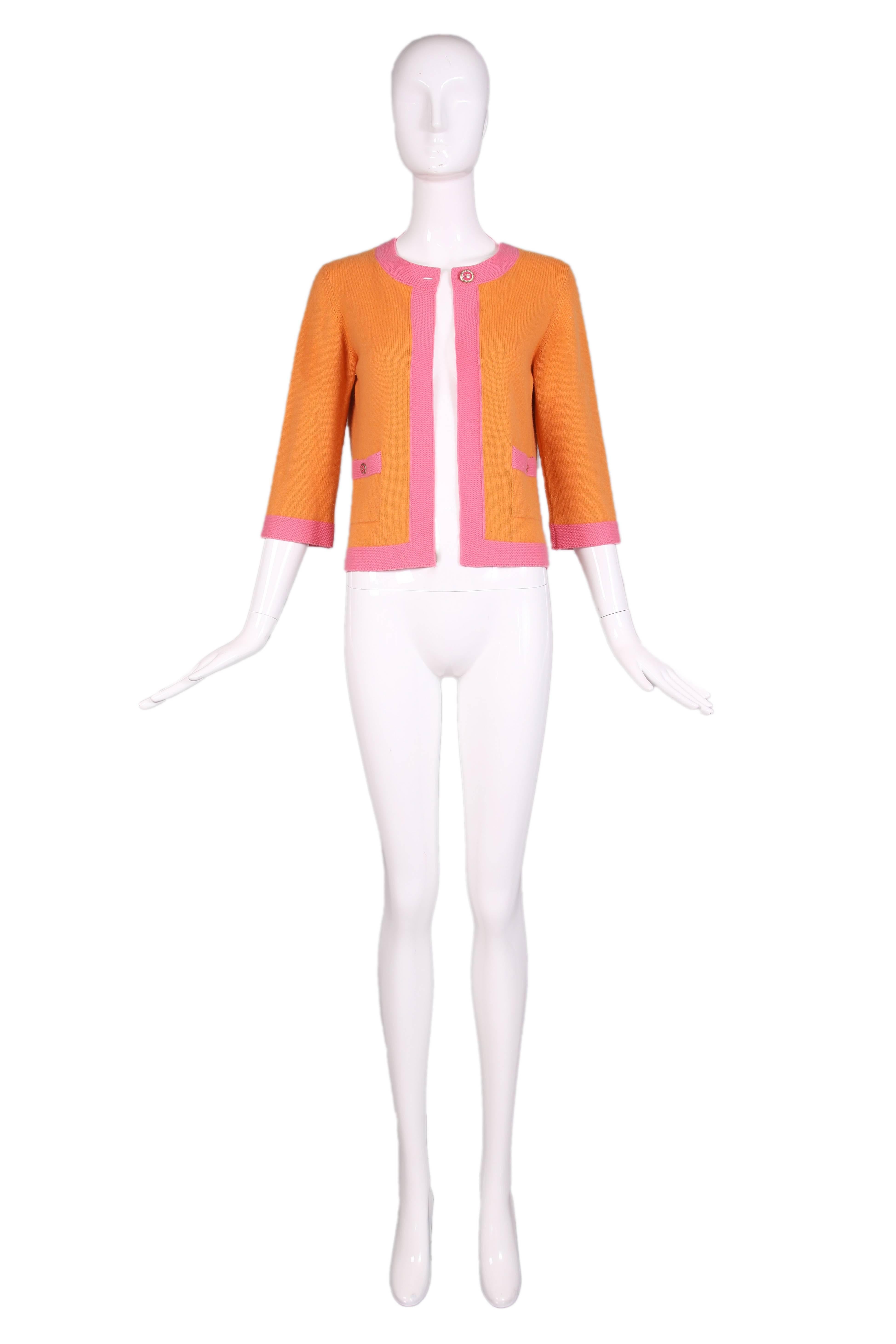 2007 P/E Chanel orange cashmere open front cardigan with pink trim. Features round pink & gold toned Chanel CC Logo buttons at top closure and at two front pockets. In excellent condition. Size EU 38.
MEASUREMENTS: (approx. measurements with panels