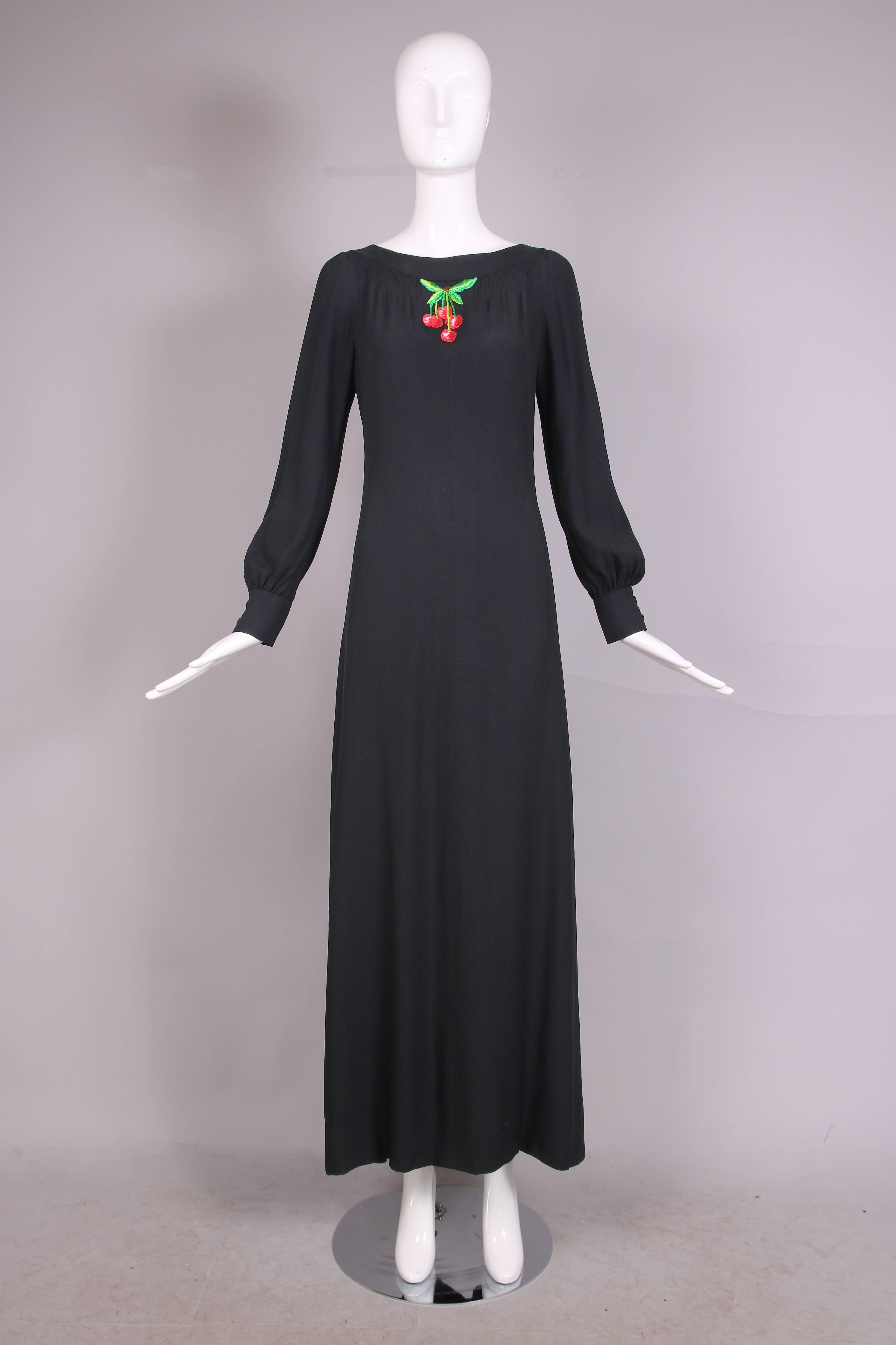 1970's Valentino A-line black crepe maxi dress with dramatic side slit. Features pin tucking detail at boat neck and an embroidered single cherry cluster applique. Cuffs each have a two black fabric-covered button closure. In excellent condition