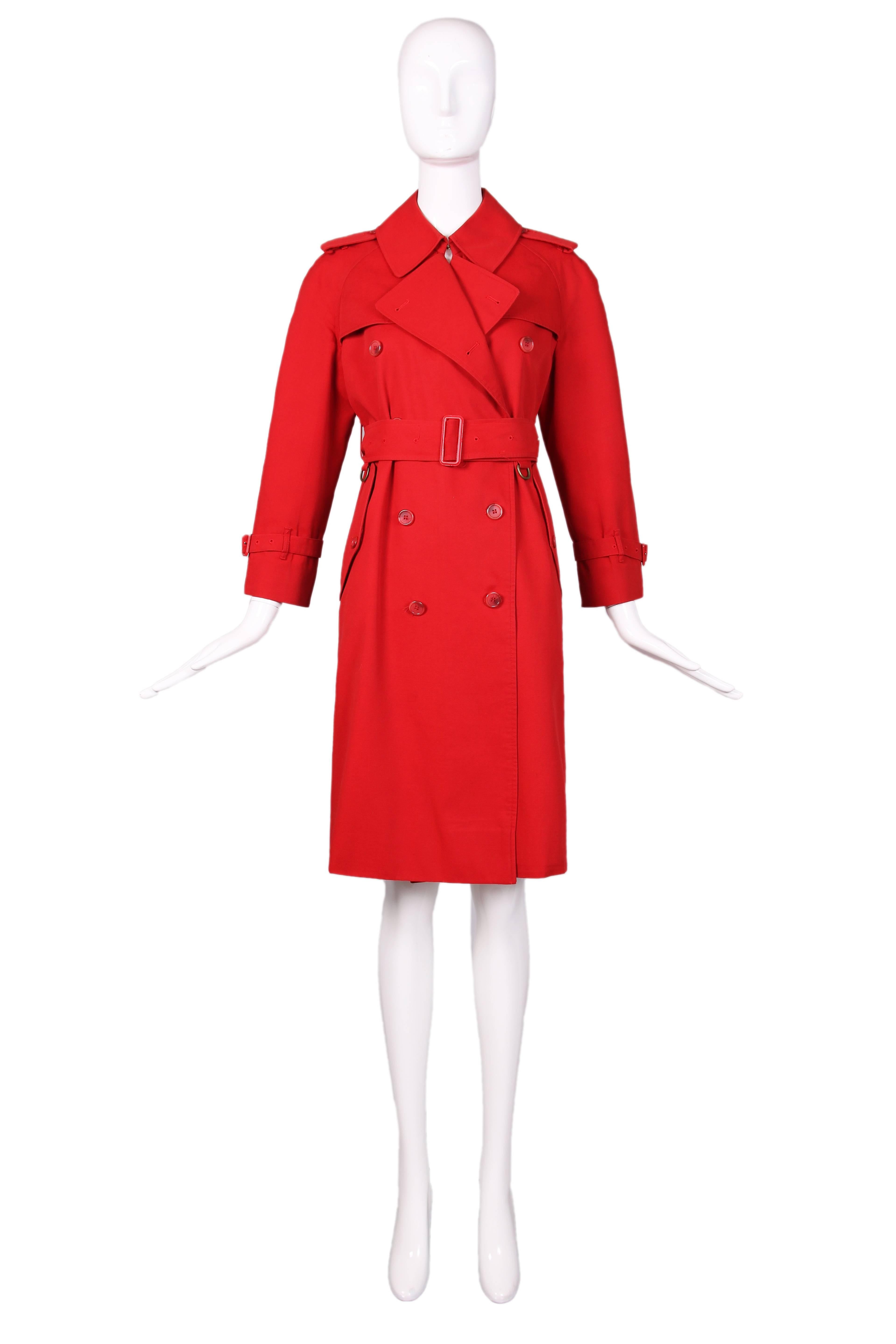 Classic Burberry red trench coat with nova check lining. Cotton blend, double-breasted coat with belted cuffs, plastic buttons, and two side pockets. Matching waist belt is detailed with metal D-rings. In excellent condition with a few unnoticeable
