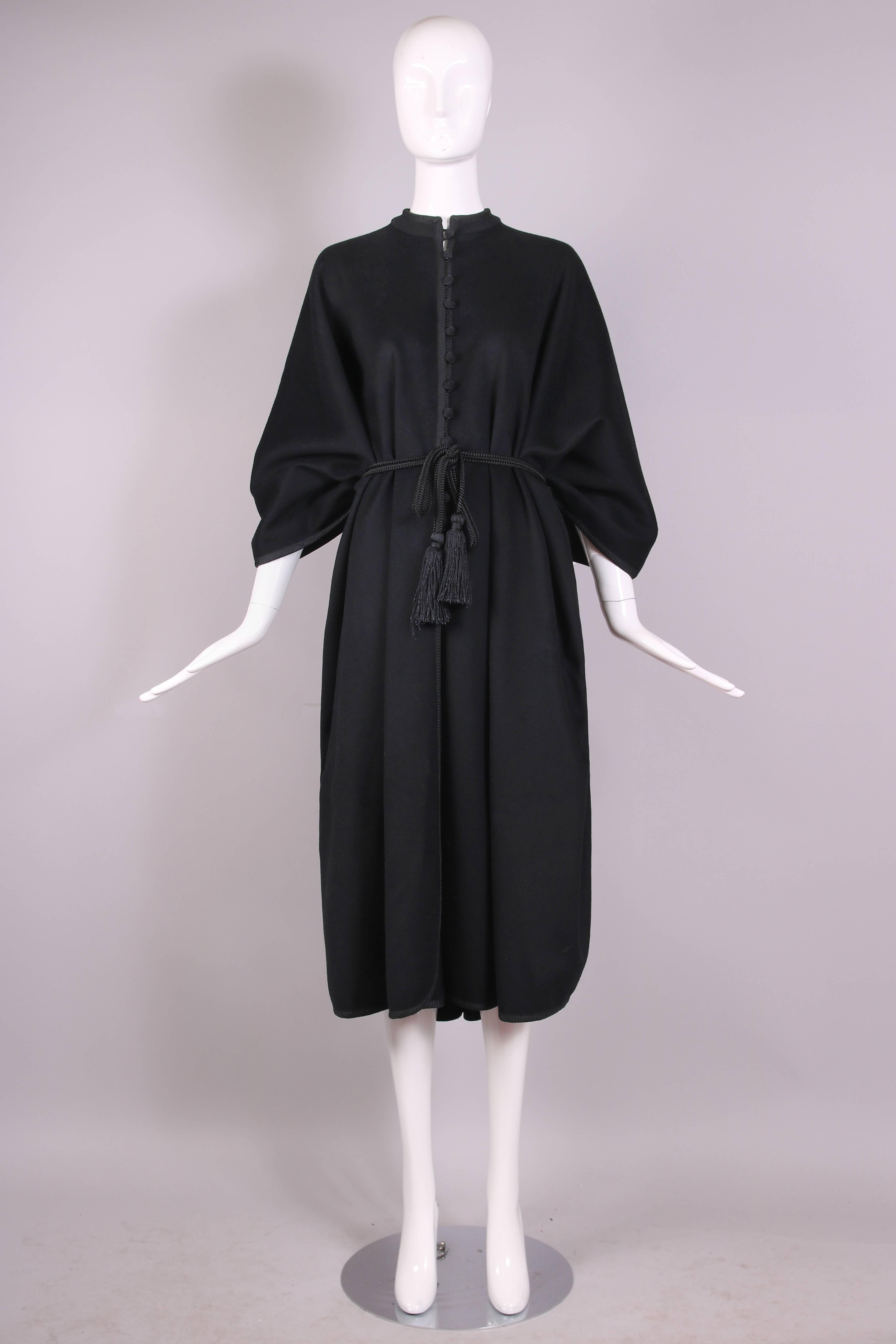 Ca. 1979 Yves Saint Laurent black wool cape w/wool braided trim and black domed spiral cord silk buttons. Cape comes with a braided silk cord that has silk tassels at either end and that wraps around the waist. In excellent condition. Size EU 40.