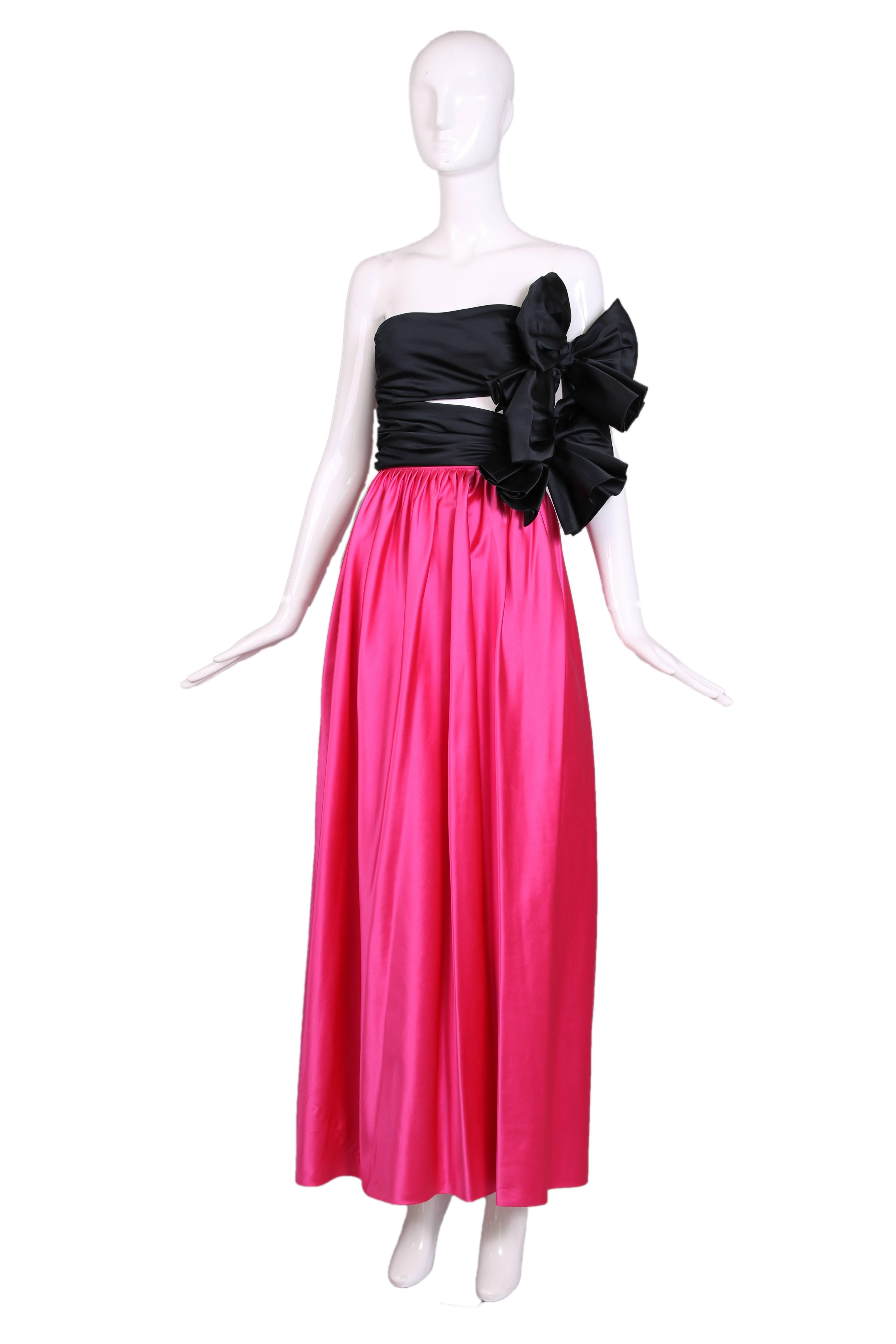 A 1979 Lanvin haute couture strapless evening gown comprised of a shocking pink satin floor length skirt and a  black satin bodice made from two horizontal ruched bands which fasten at the side and feature two dramatic oversized bows. The skirt is
