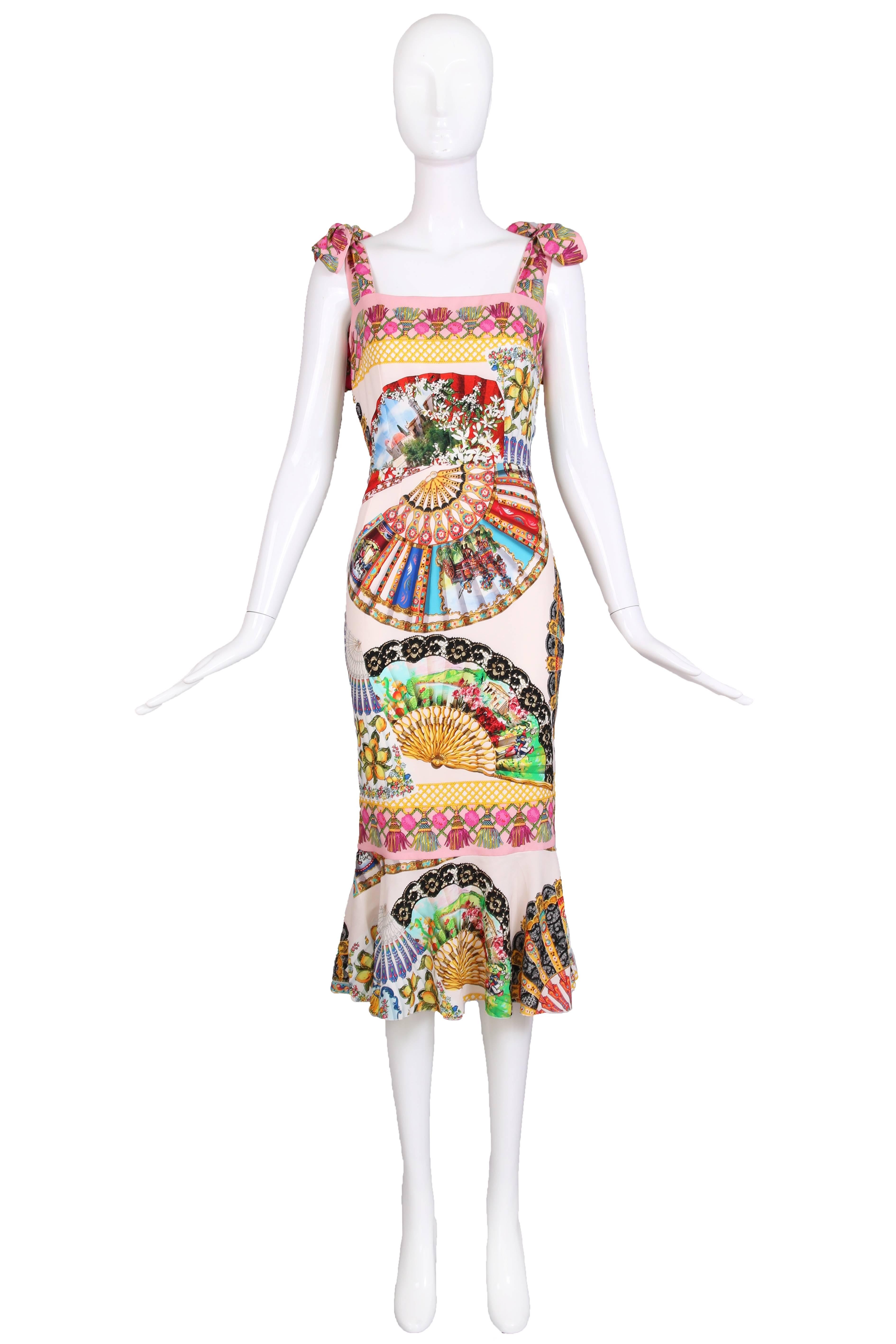 Dolce & Gabbana silk cocktail dress with shoulder straps that tie in bows, a square neckline and trumpet hem. Dress features a multi-colored graphic scenic print dominated by vintage hand fans, tassels, vignettes of Italy, lattice work and