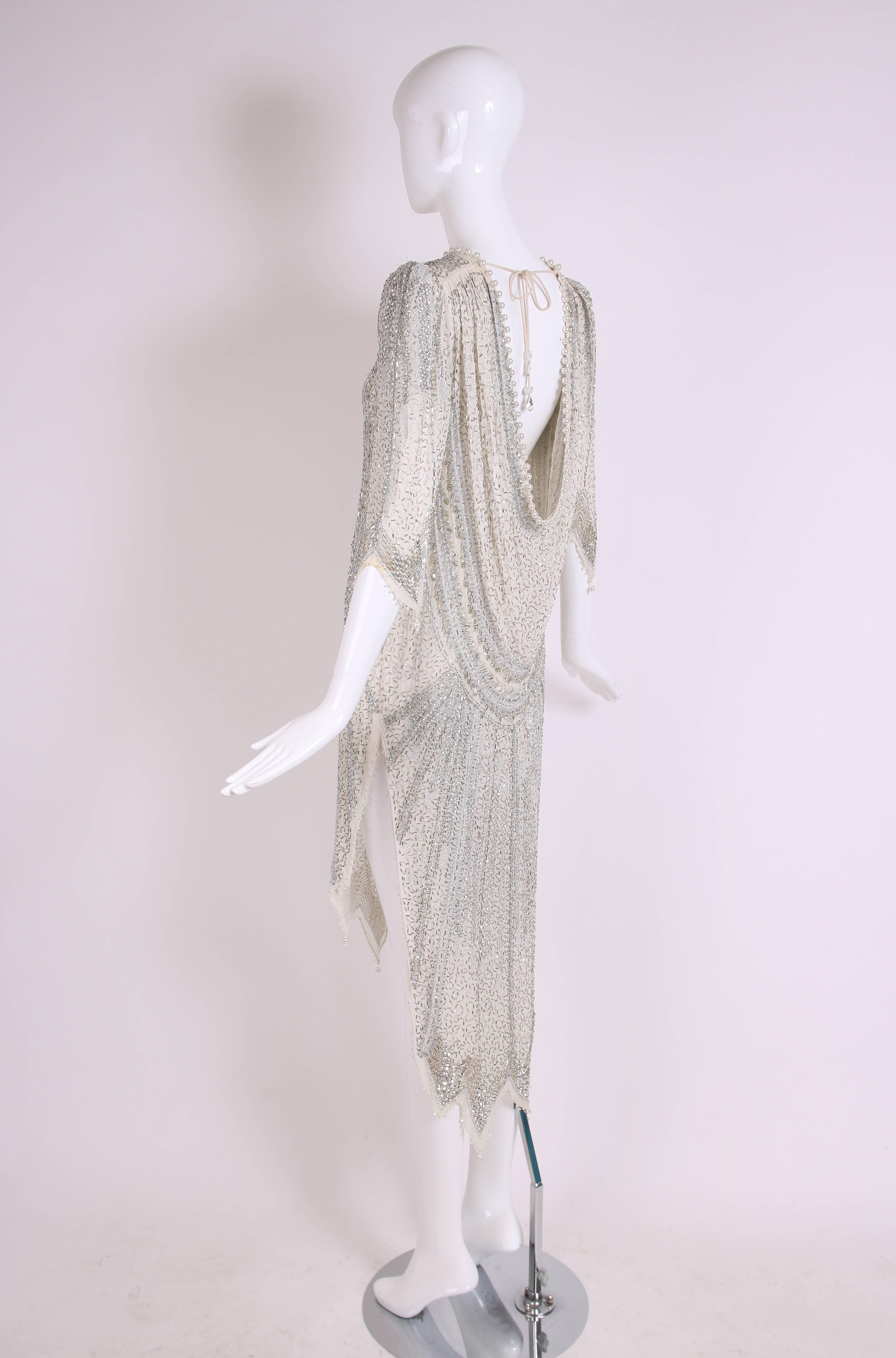 Vintage Zandra Rhodes elaborately beaded and sequined evening dress with 3/4 sleeves, pearl trim, dramatic side slits, open back and high-low hem from back to front. Beads are silver and fabric is a sheer chiffon in a pale blue/creme hue. Gown is in