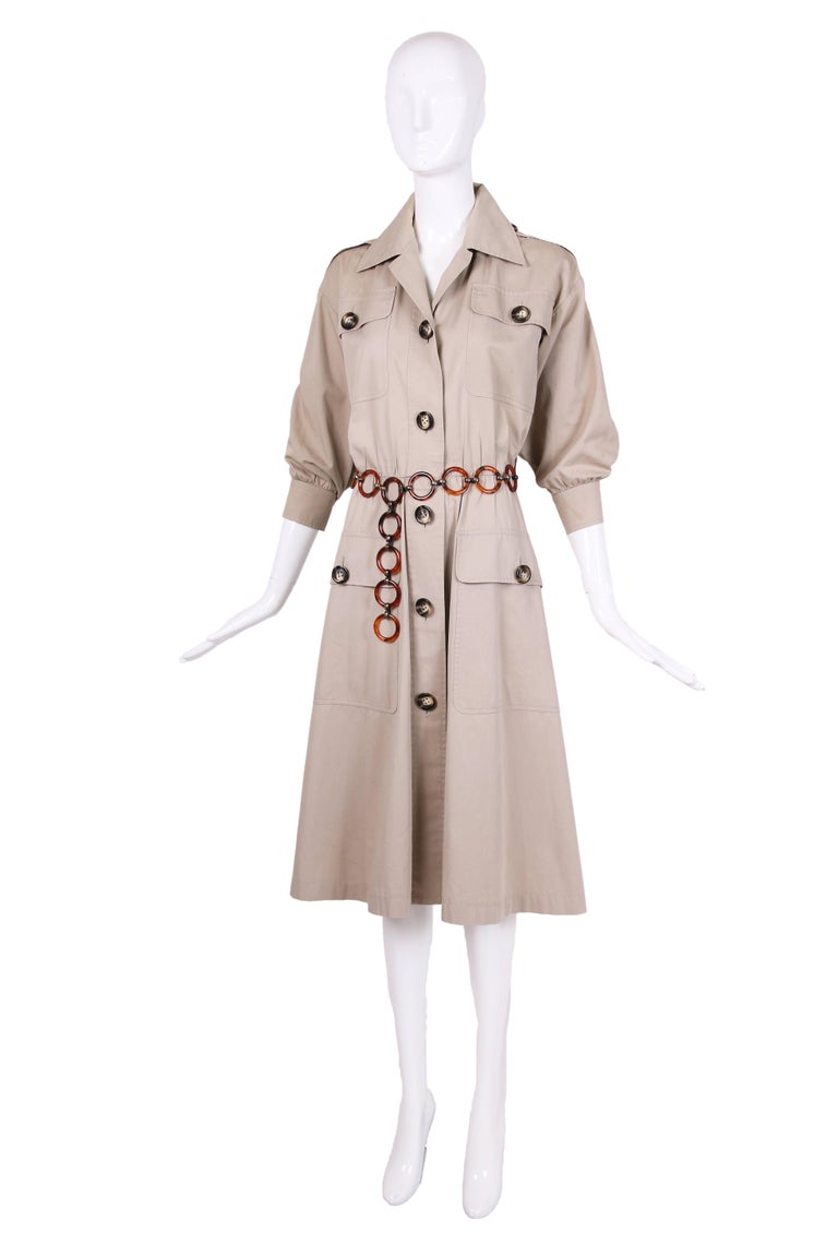 1970's Iconic Yves Saint Laurent safari coat/dress with oversized button closures, 3/4 sleeves, gathered waist and oversized frontal pockets. Comes with tortoise shell circle belt. In very good condition with some tiny spots & marks on both sleeves