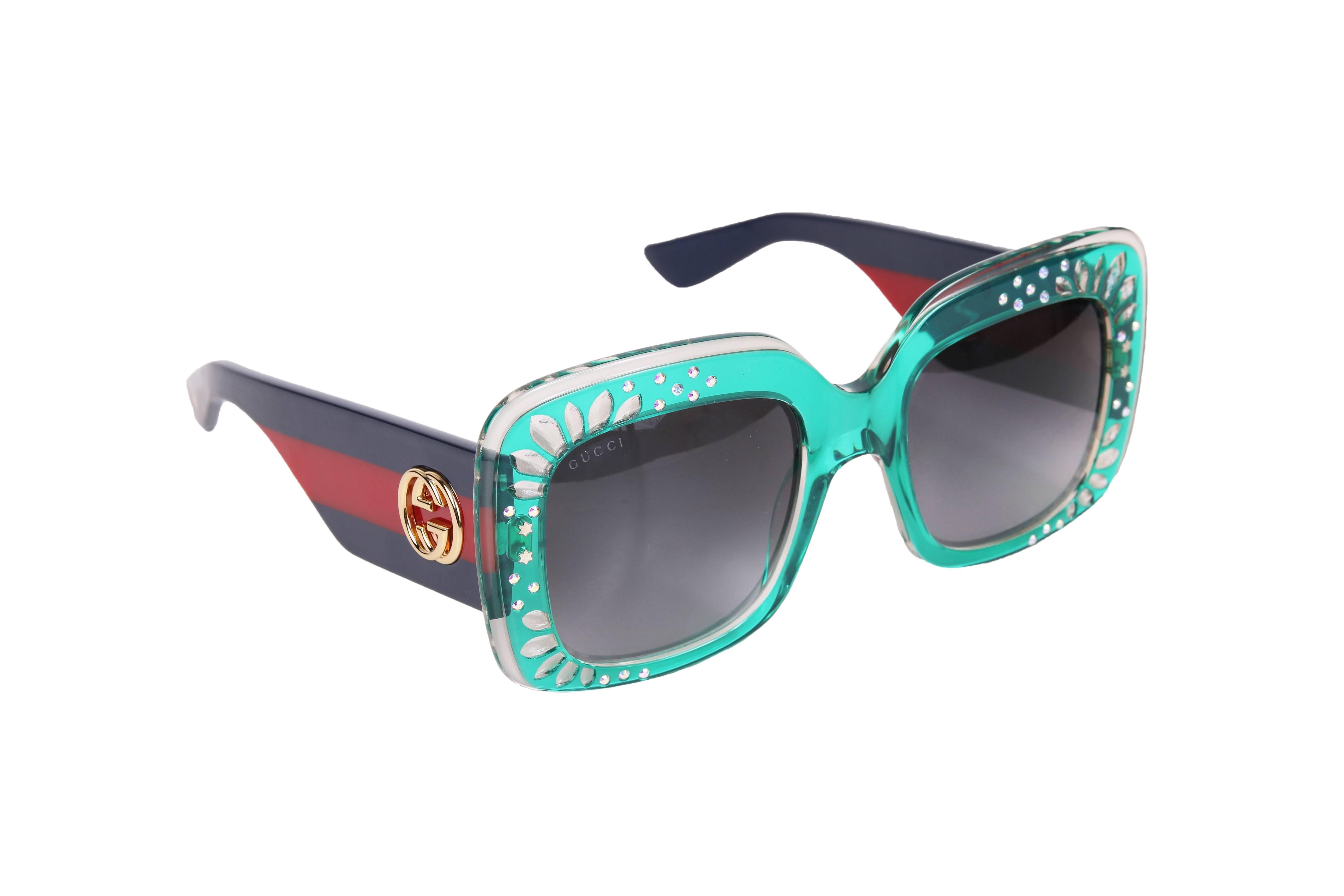 Gucci oversized square frame sunglasses in green acetate with etching detail at the frame as well as some rhinestones and stars. The sunglass arms are made of acetate and feature the iconic Gucci racer stripe in blue and red - punctuated with the