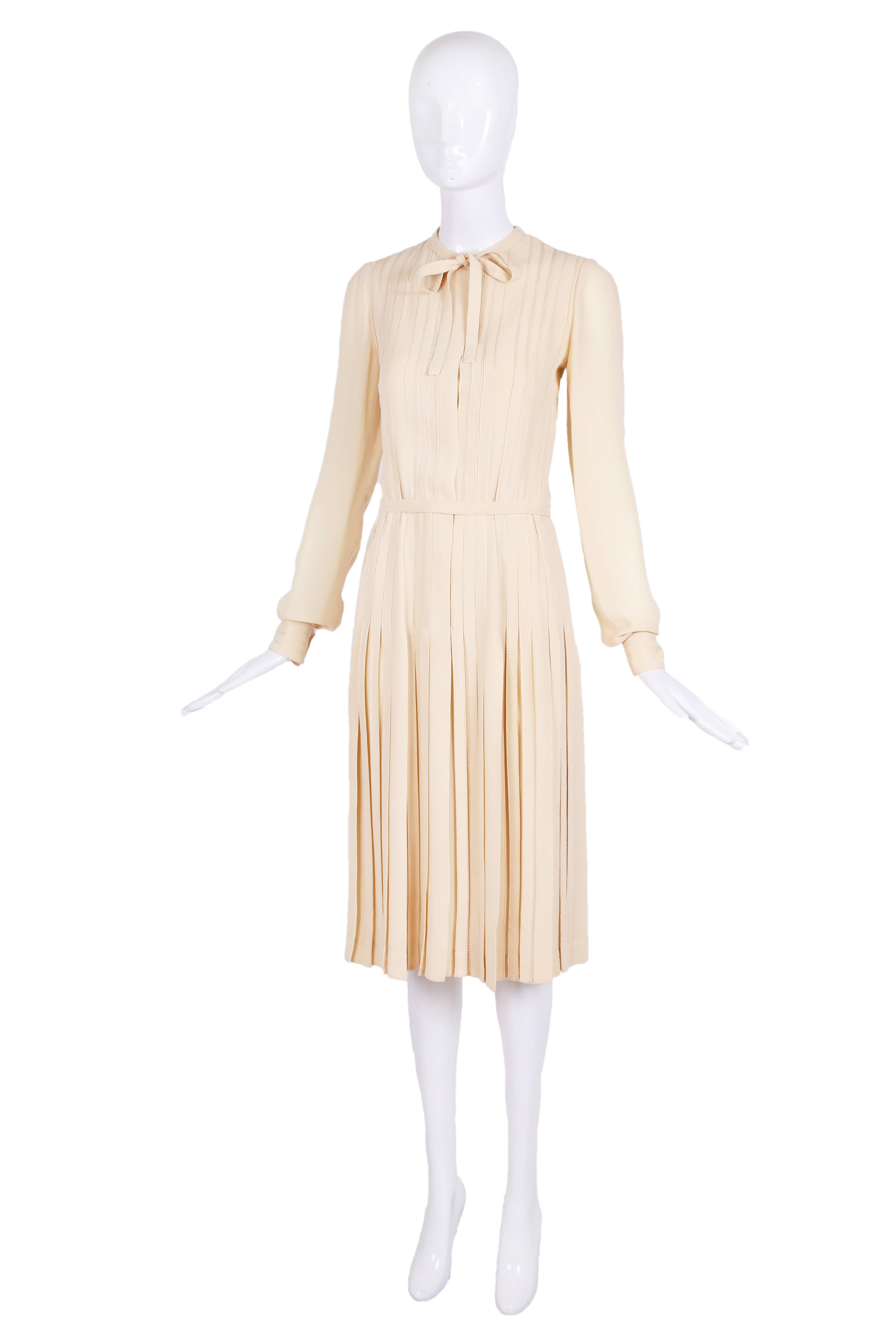 Ca. 1970 CHANEL haute couture n°49278 creme colored silk crepe long-sleeved day dress with overstitched pleating detail at the bodice and drop-pleated skirt. Details include ties at the neck, a self belt, hidden fabric colored snaps and button