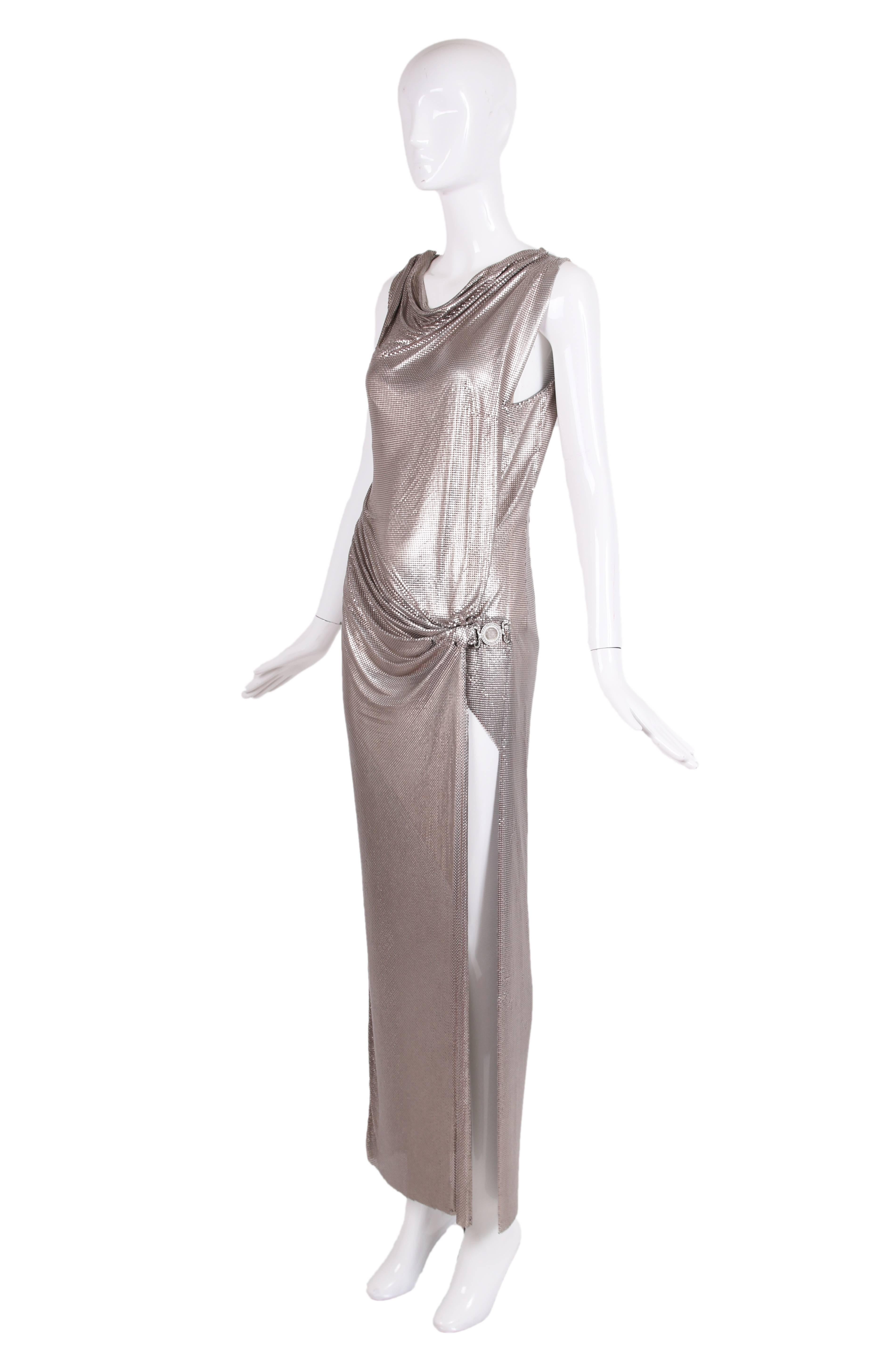 1998 S/S Gianni Versace couture label Oroton silver chainmail sleeveless gown with draping at the front right which culminates in a clear medusa medallion located at left/thigh-high slit. In excellent condition. Labeled at bodysuit located at