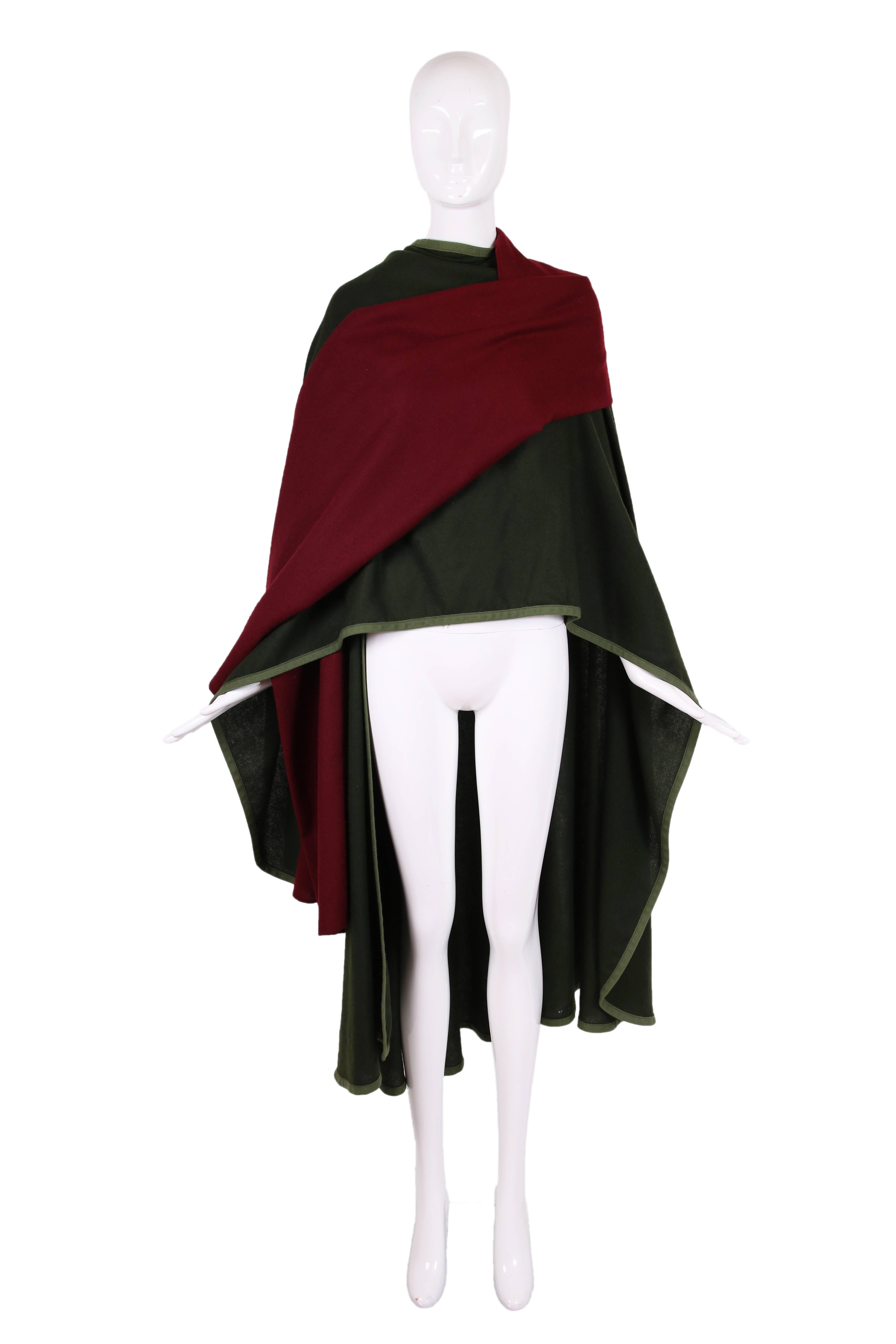 1970's Yves Saint Laurent YSL hunter green & burgundy wool cape with light green wool trim. The cape is constructed from a piece of green wool that folds over the shoulders, forming a panel down either side of the body front. Attached at the