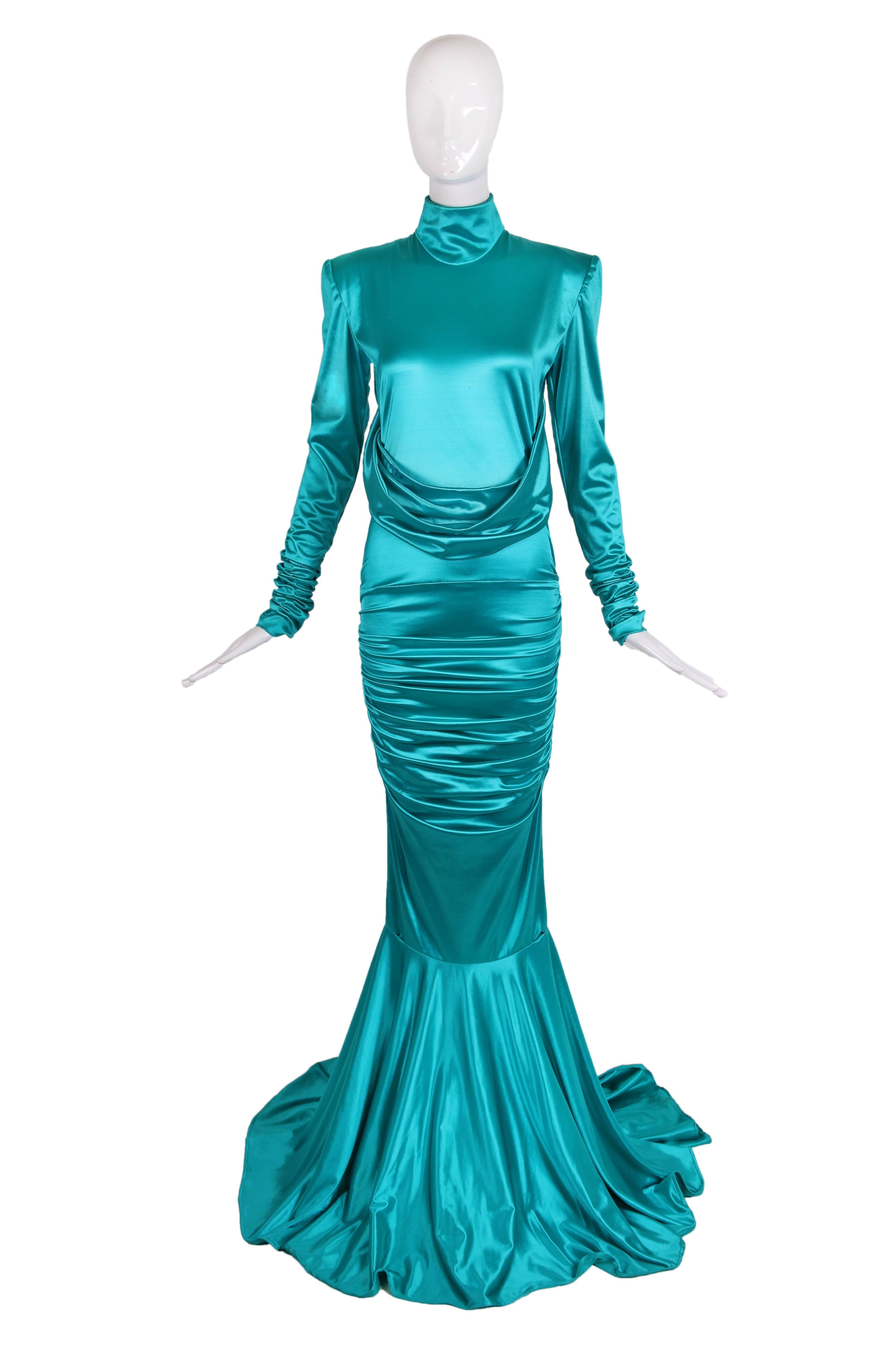 1988 Patrick Kelly turquoise stretch mermaid gown with high collar, crossed swags, ruching through the hips and trained circle skirt from the knee. In very good condition with some minor pulls, lipstick marks on swags and faint stain on train. No