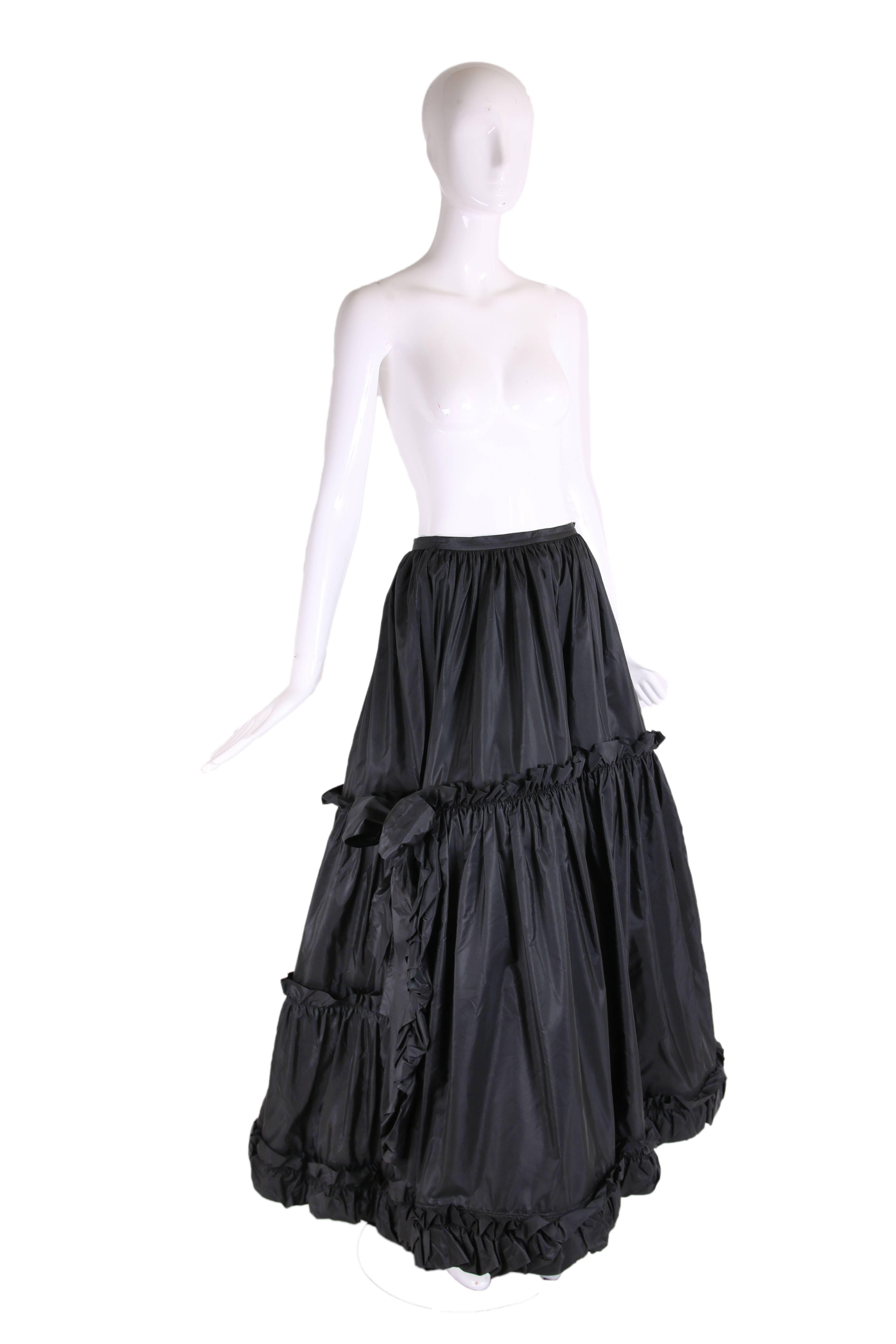 1970's Yves Saint Laurent black silk taffeta tiered skirt with silk lining, horse-hair batting, an opening at either side seam and ruffled trim at each tier. There are two silk taffeta bows just above the slits at each side seam and the back dips