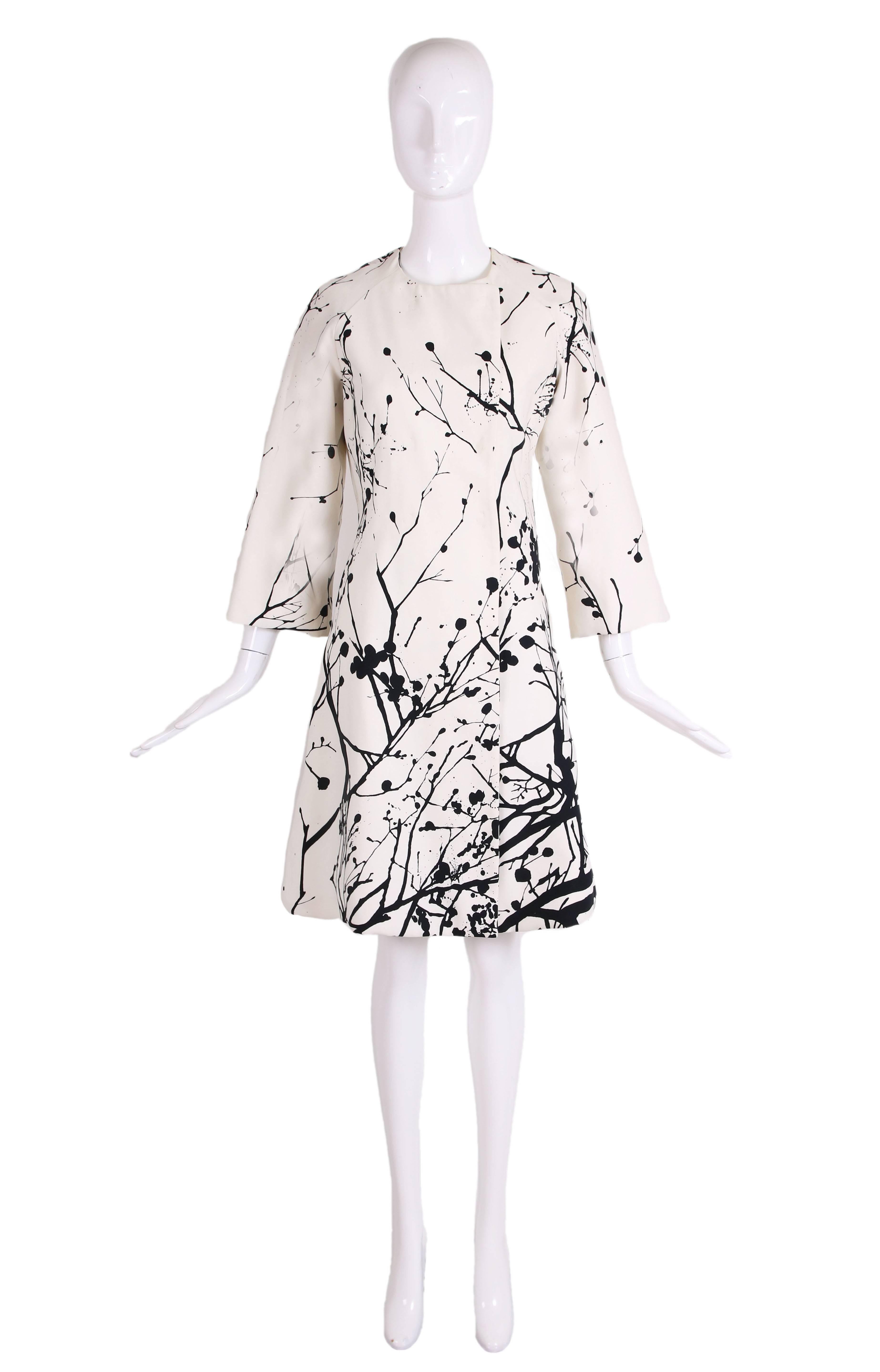 Tuleh black and white abstract coat with an abstract print suggestive of twigs and leaves. Coat fastens down the front with two sets of hidden hook and bar metal closures and features raglan sleeves. There is no fabric tag but the fabric appears to
