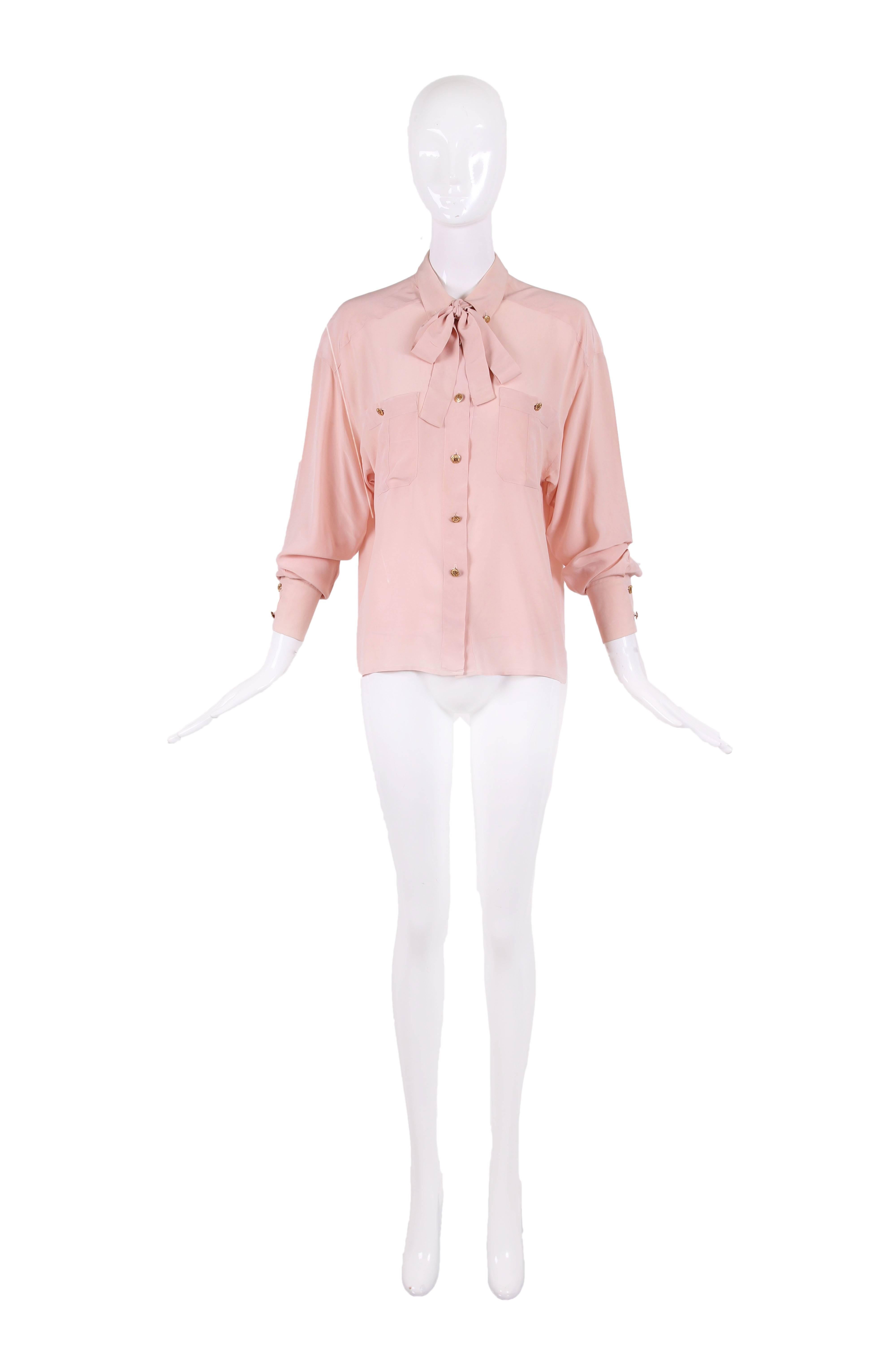 Vintage Chanel pale pink long sleeve collared button down silk blouse. This blouse has two front pockets, neck ties, and dolman sleeves. There are gold-toned 
